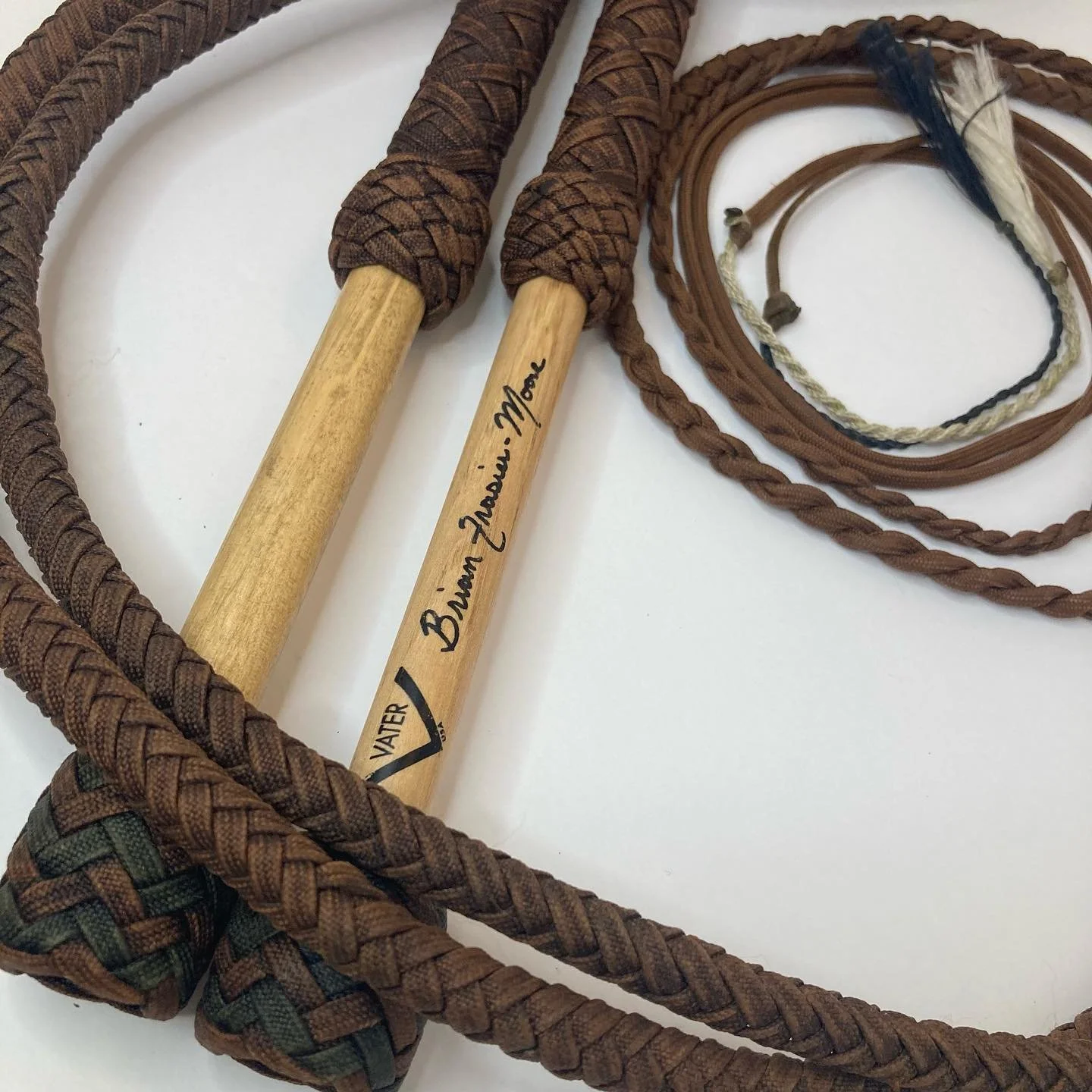 A pair of brown jump ropes with round wooden handles, one handle has a signature and other markings, along with several braided leather and fabric cords.