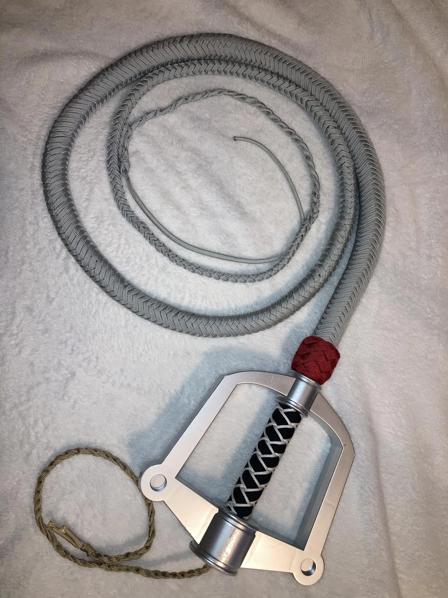 A metal and braided fabric device with a red wrapping, accompanied by a black and white lanyard, placed on a white textured surface.