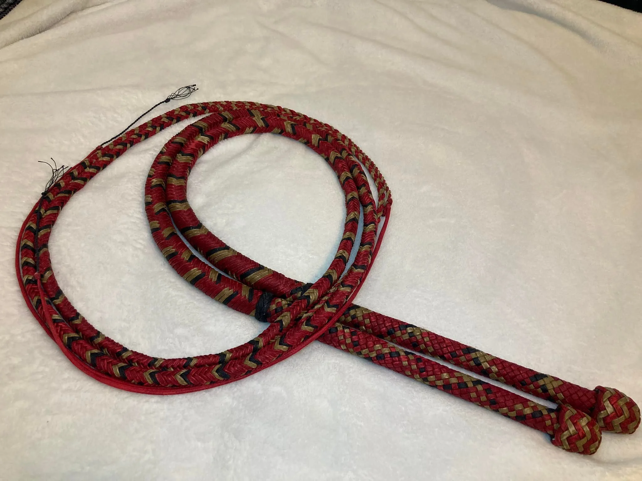 A pair of red and black climbing or gymnastics ropes with some frayed ends, lying on a white fabric background.