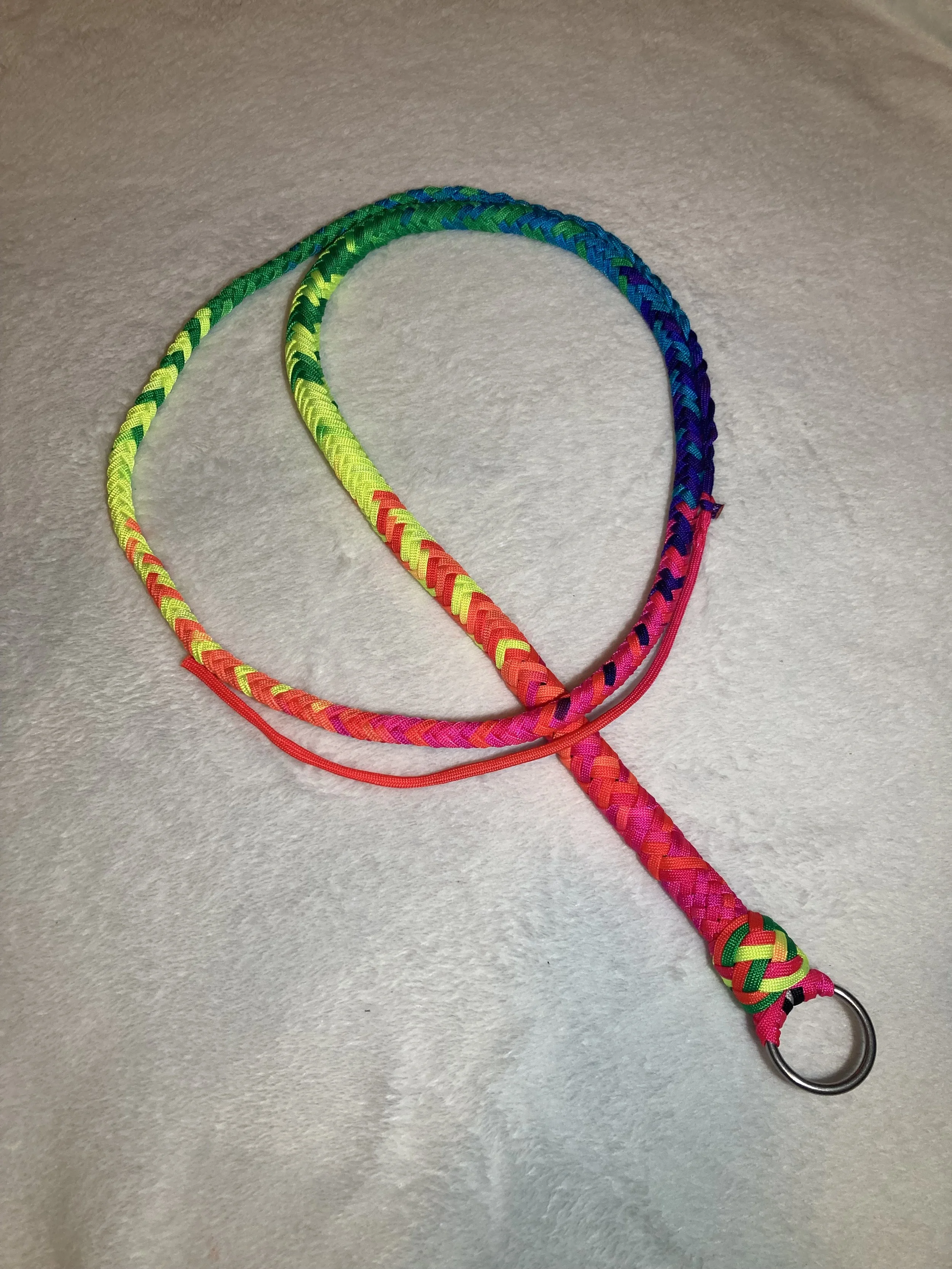 Colorful braided lanyard with a metal ring at the end, placed on a light-colored textured surface.
