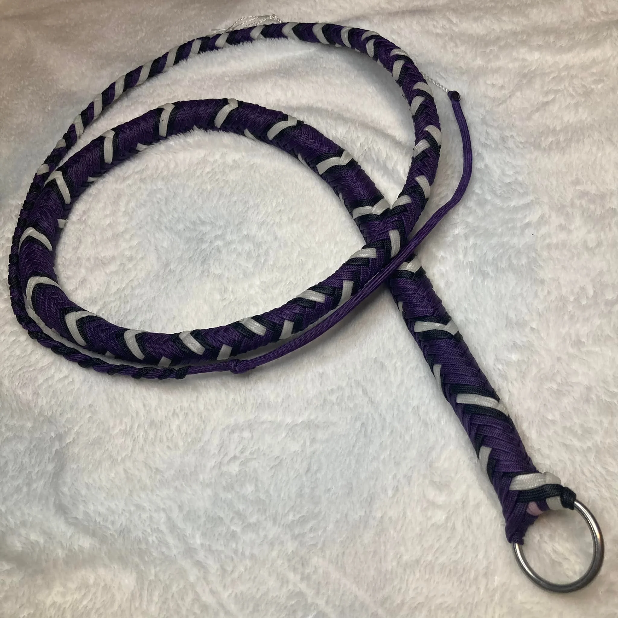 Purple and black braided leash with a metal ring at one end, placed on a white textured surface.