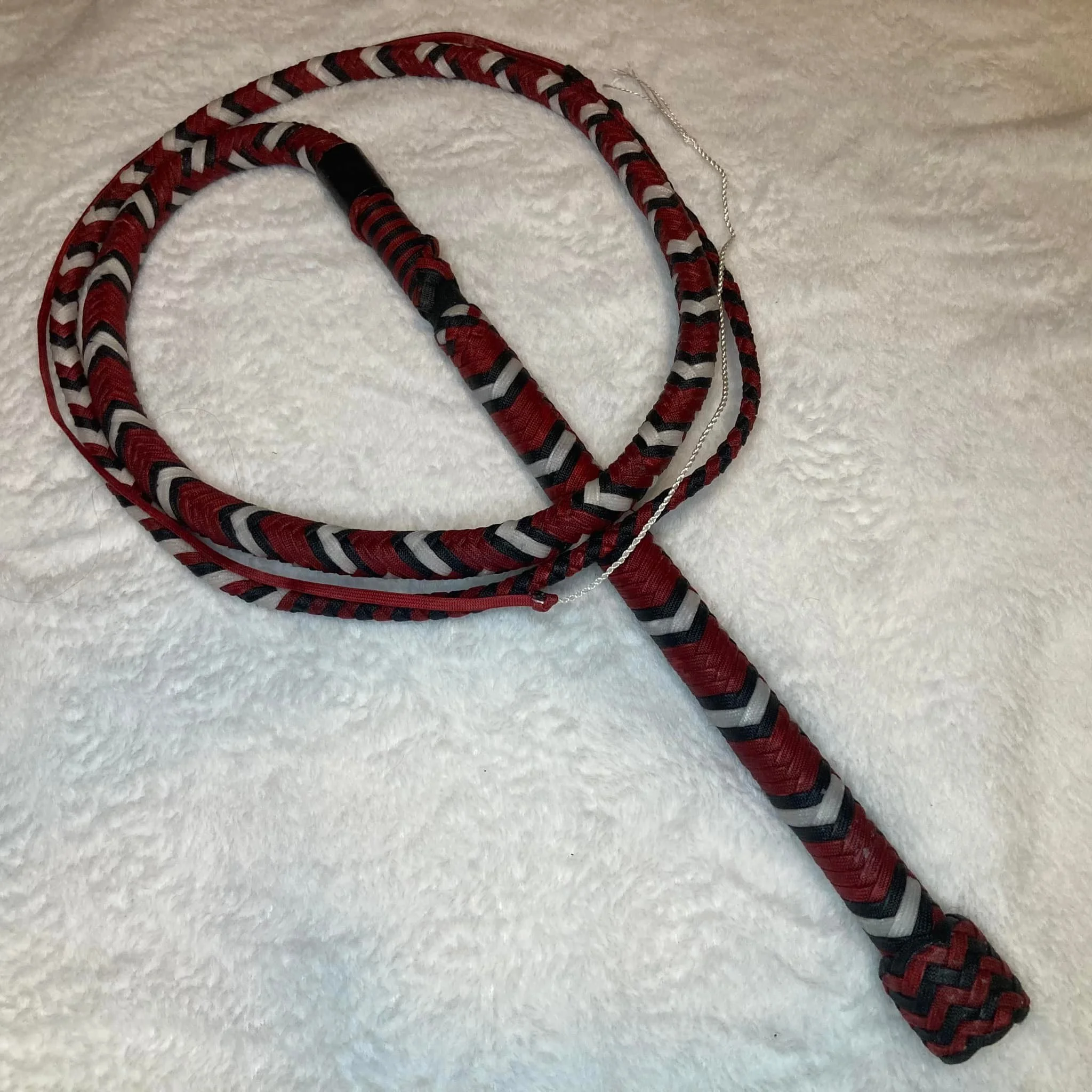 A coiled whip with a red, black, and gray braided pattern resting on a white textured surface.