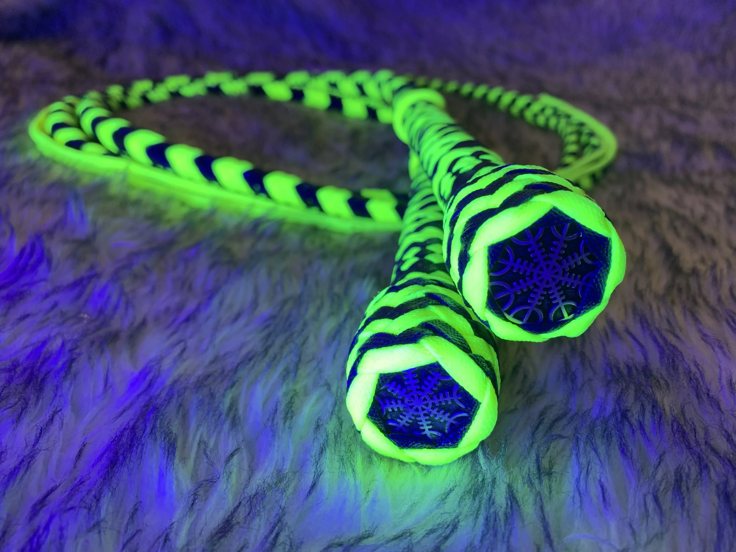Glow-in-the-dark neon-colored snake necklace with a green and black striped pattern, lying on a shaggy surface with fluorescent purple lighting.