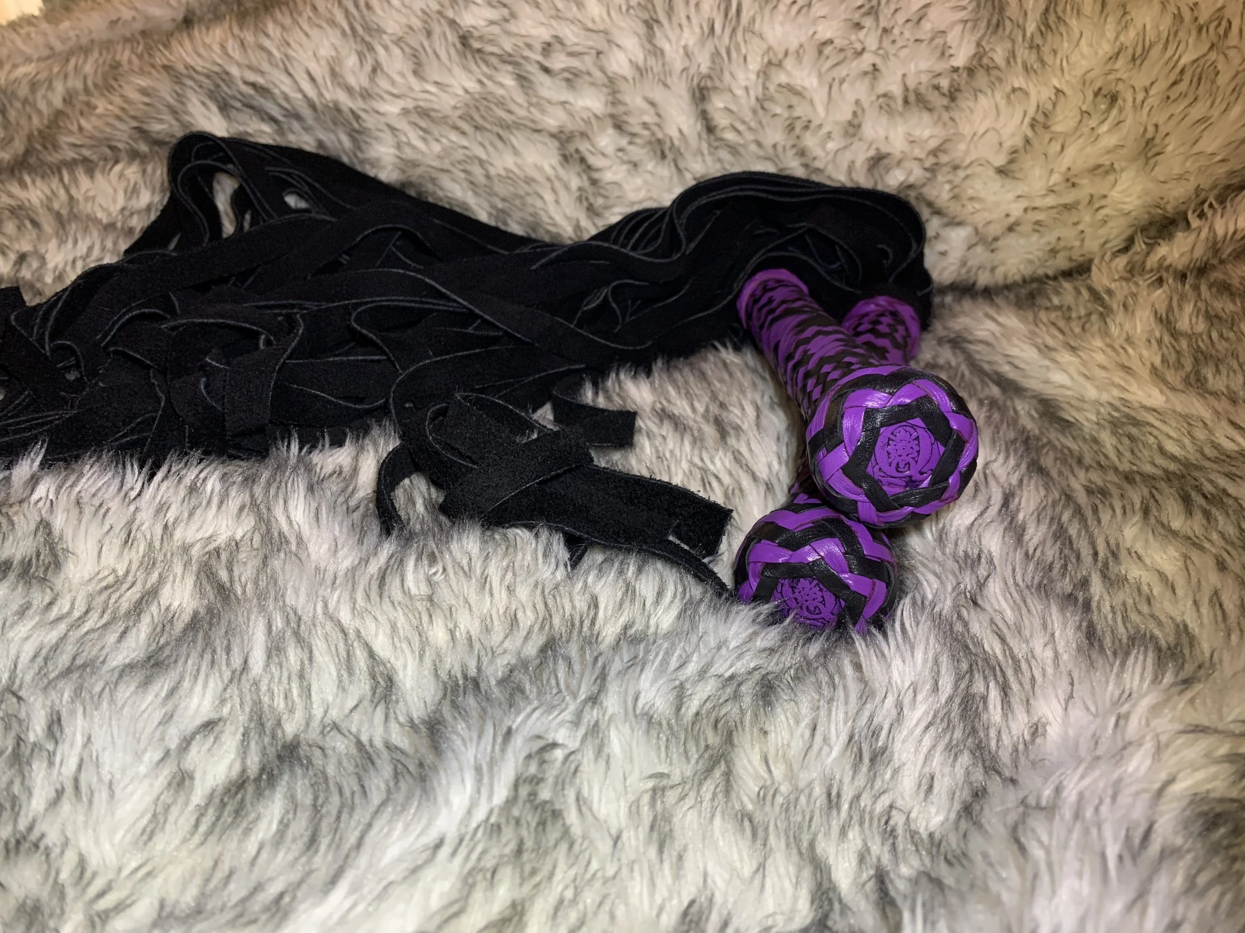 Twin 3' suede floggers with custom braided handles in black and purple kangaroo leather highlighting the stamped leather coin in the hilt.
