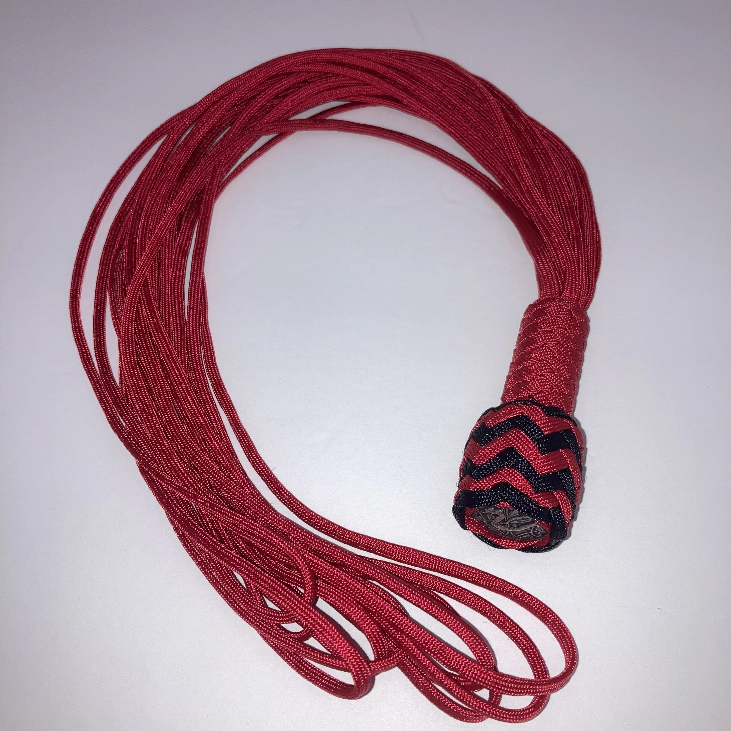 Red braided cord with decorative black and red woven end piece on a white background.