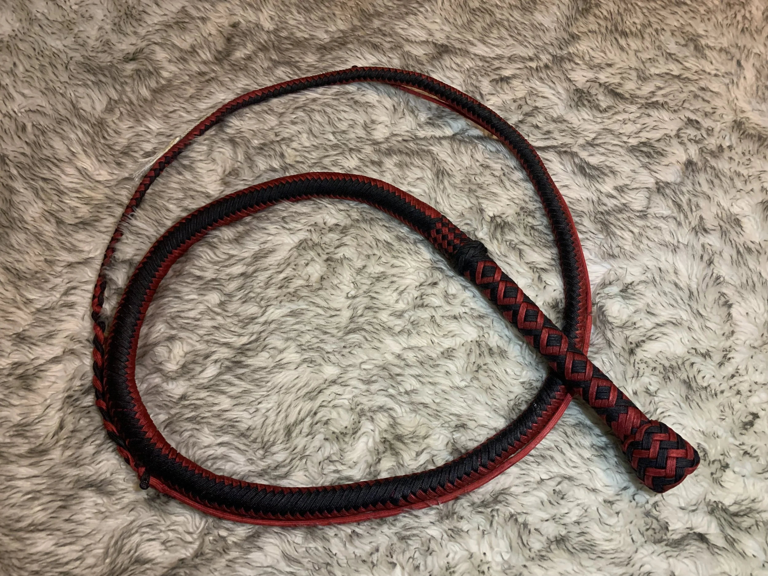 A black and red braided dog leash on a gray furry surface.