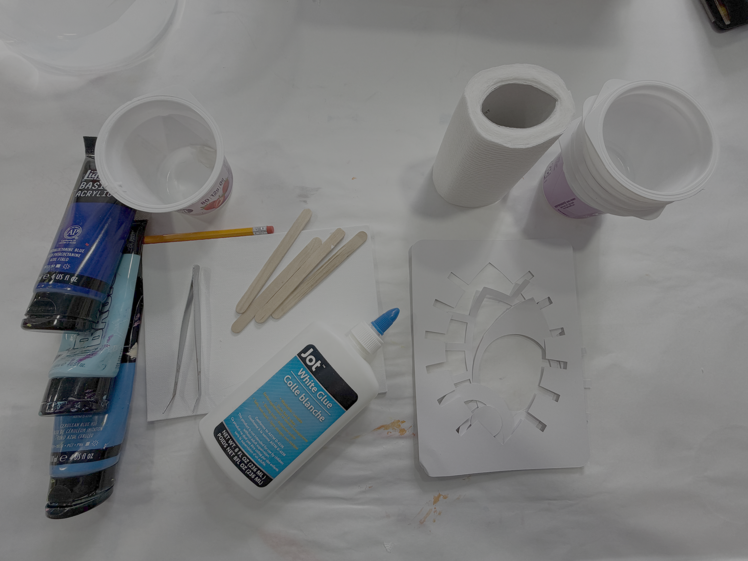 Toilet paper art supplies including acrylic paints, white glue, tweezers, canvas, eye stencil, pencil, mixing sticks, and cups.