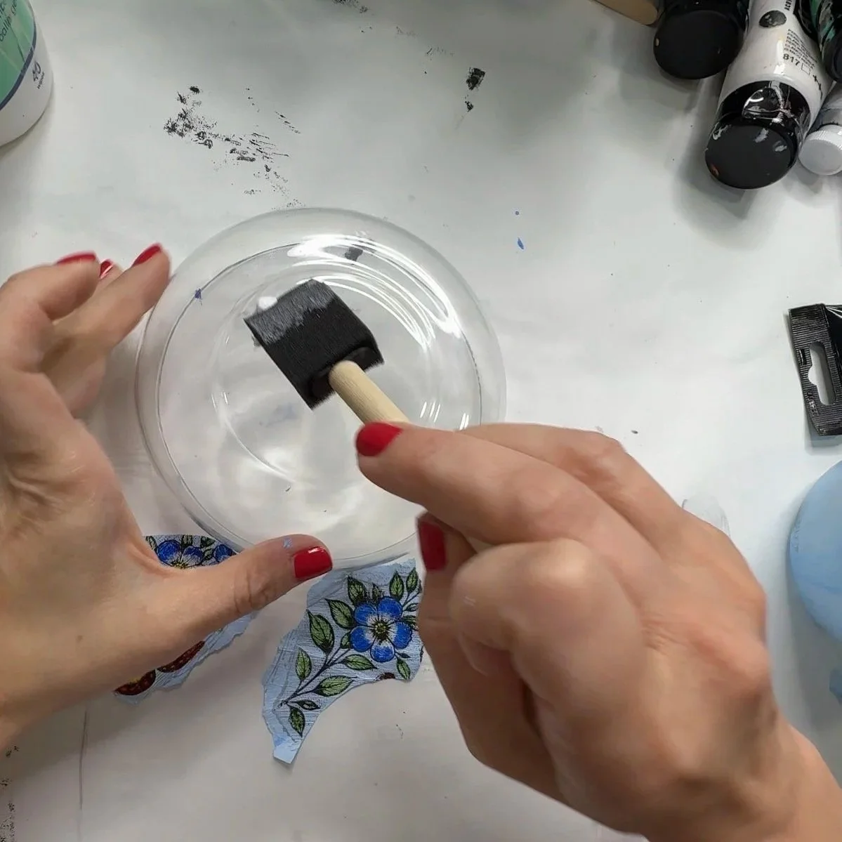Foam brush spreading a thin layer of Mod Podge inside a glass bowl before decoupage