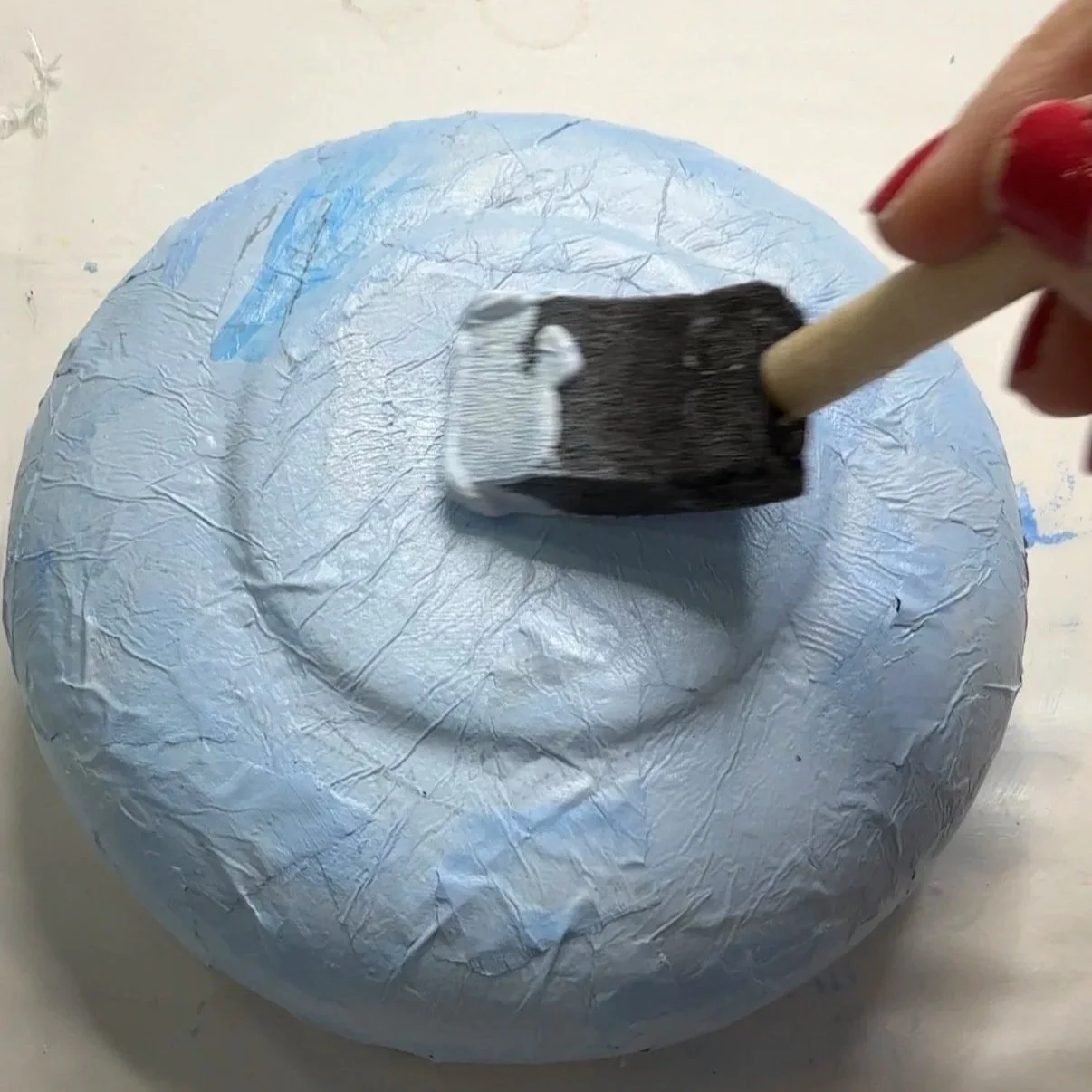 Sealing a finished decoupaged tissue paper bowl with a final coat of Mod Podge