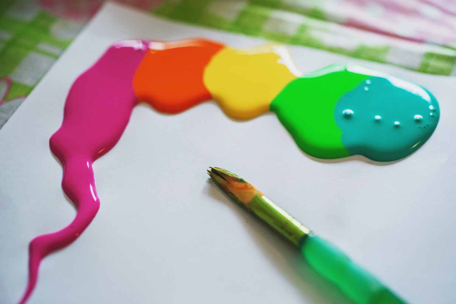 Five blobs of colorful acrylic paint squeezed onto paper next to a paintbrush