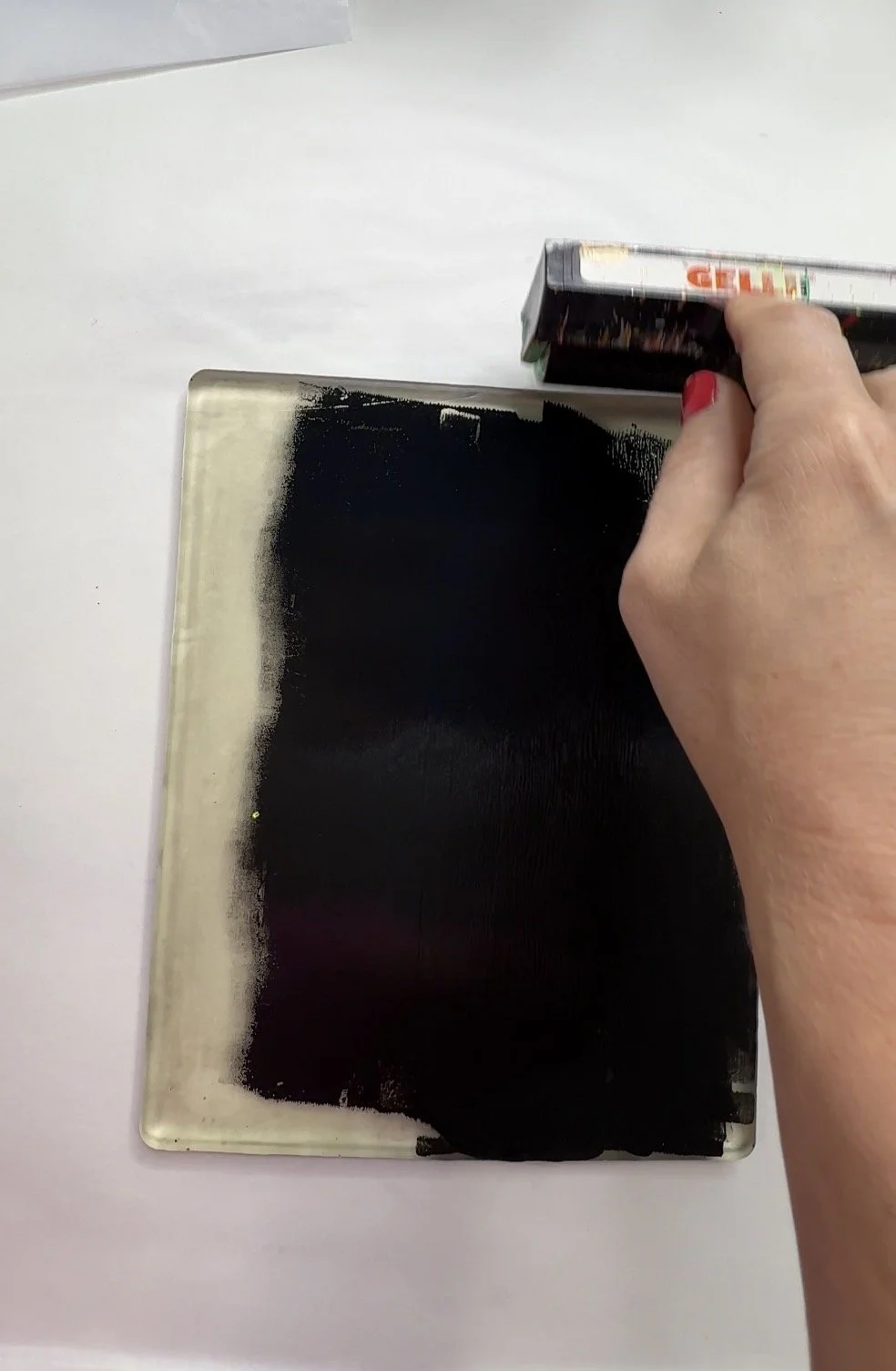Brayer spreading an even layer of black acrylic paint across a gelli plate before an image transfer