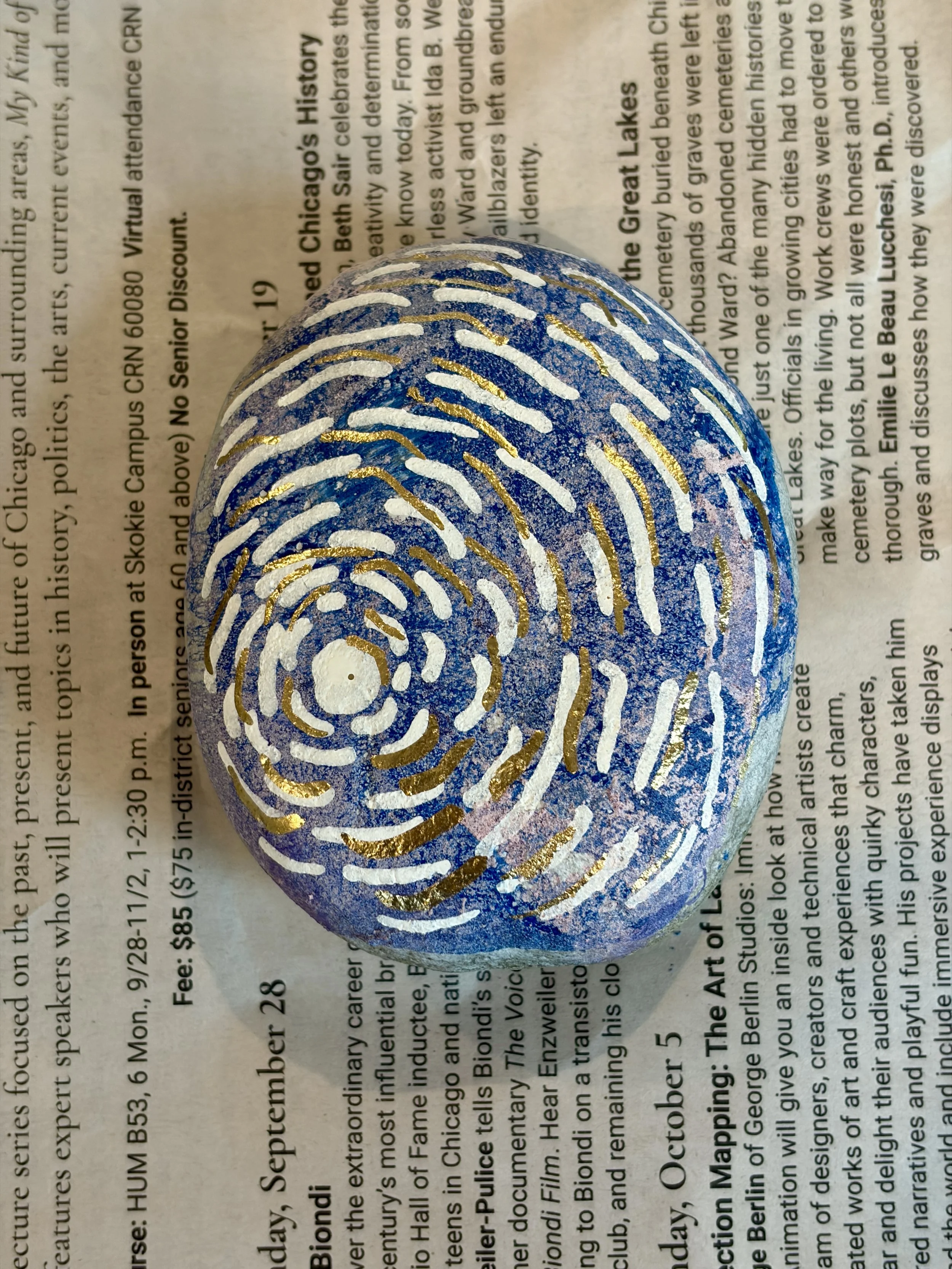Hydro dipped rock decorated with a gold and white spiral swirl design using a dotting tool