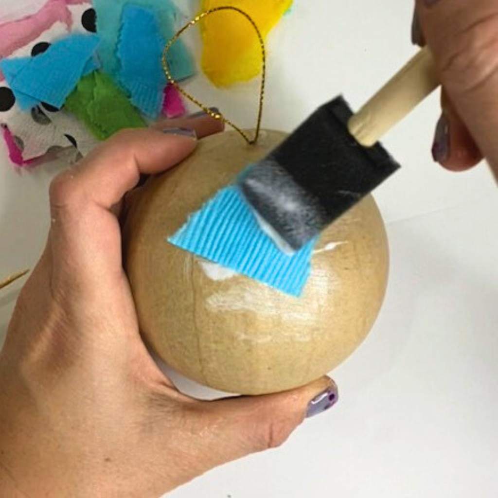 Smoothing a napkin piece onto a paper mache ornament with Mod Podge