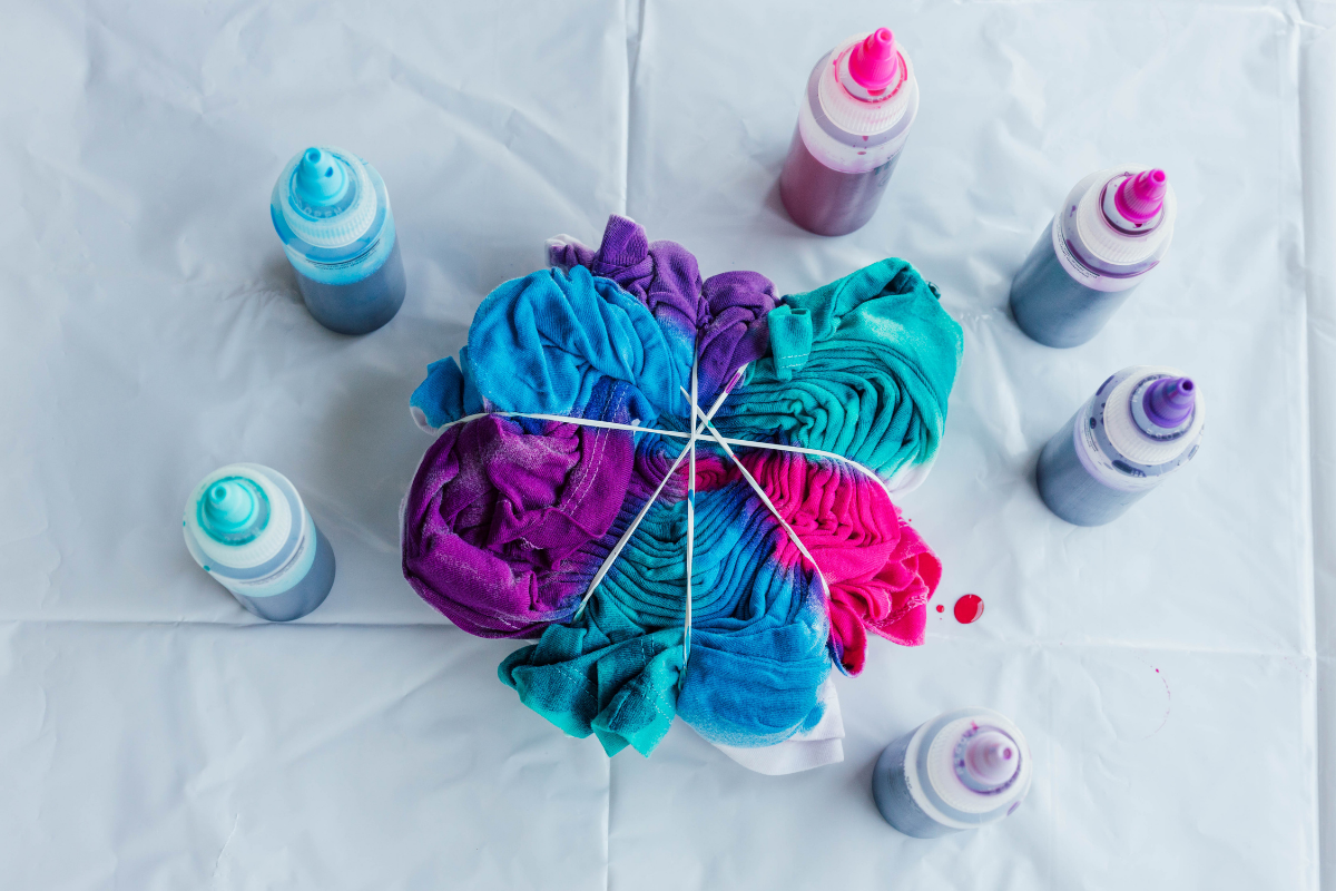 Brightly colored tie-dye shirt folded with rubber bands surrounded by squeeze bottles of fabric dye