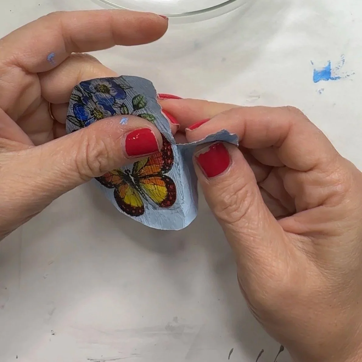 Hands tearing a gelli-printed butterfly tissue paper piece into small sections for decoupage