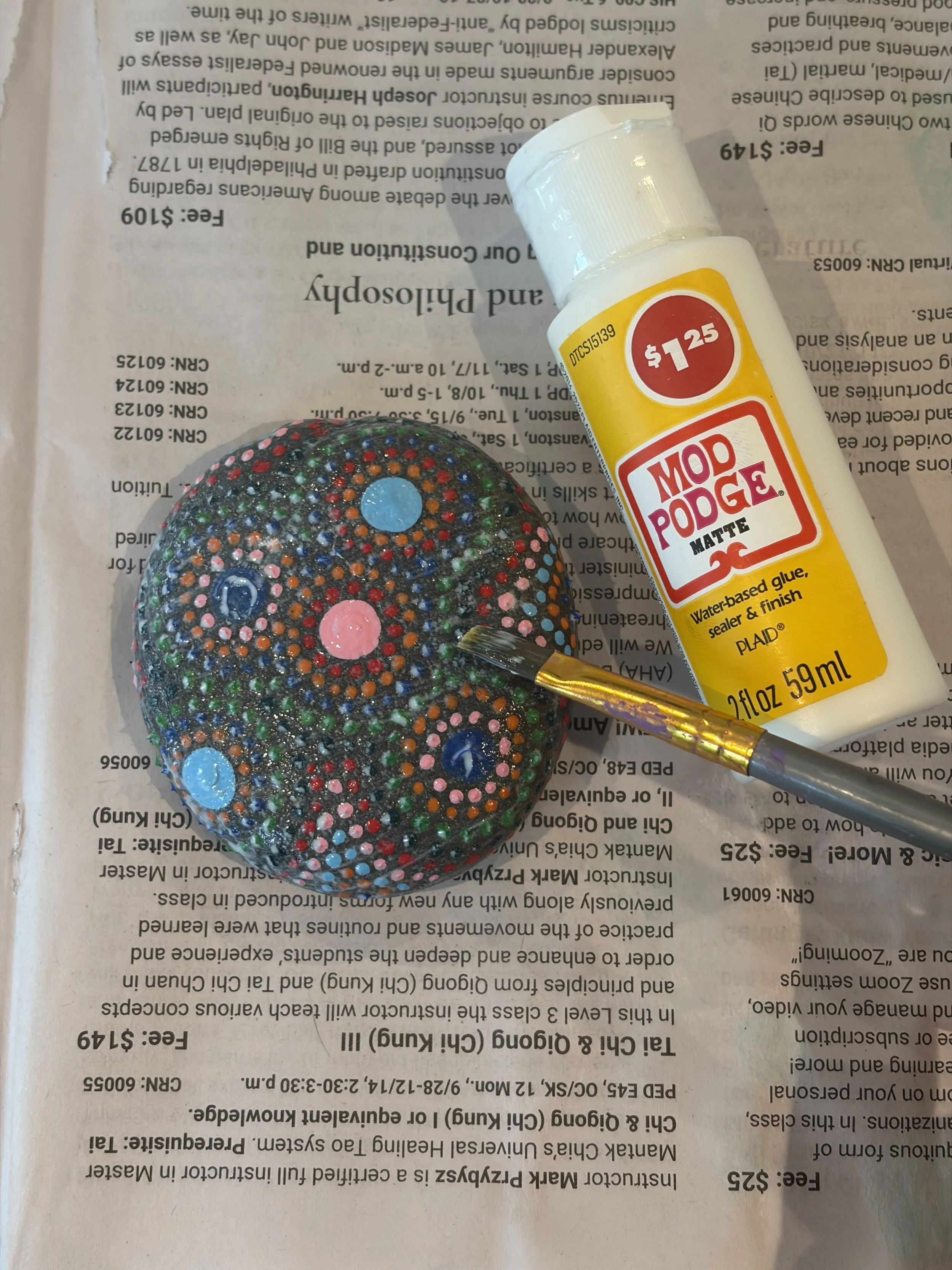 Mandala dot-painted rock being sealed with Mod Podge before outdoor garden display