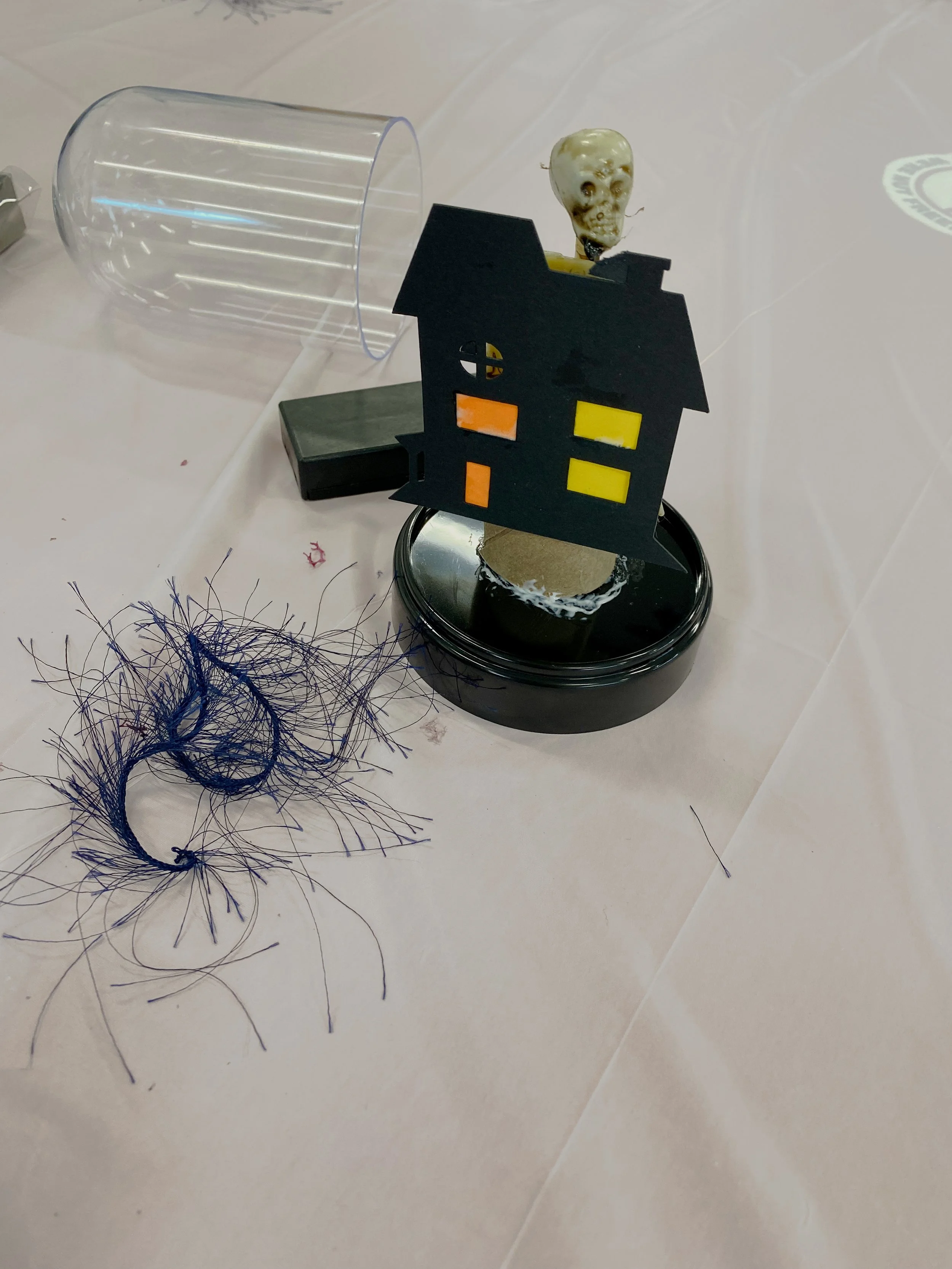 Mini haunted house, skeleton, moss, and plastic cloche dome arranged for a DIY Halloween cloche