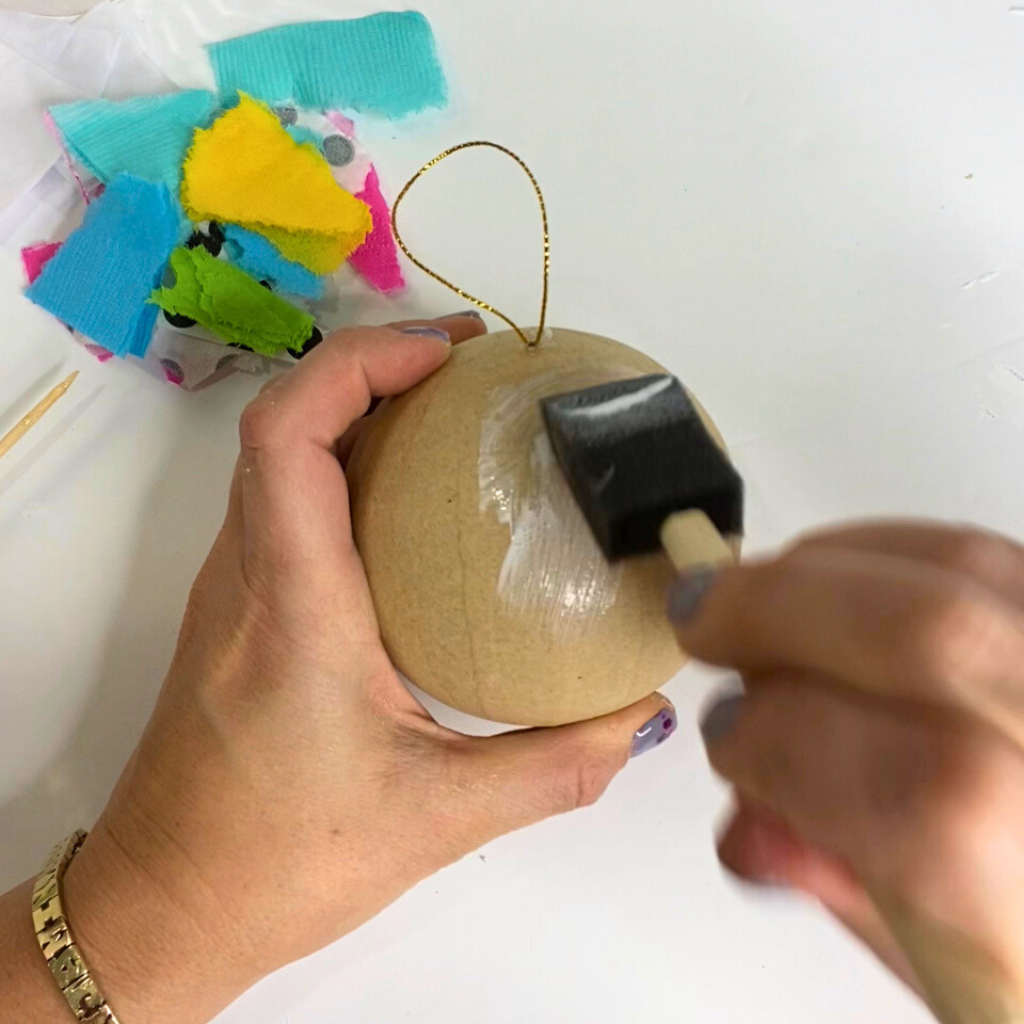 Brushing Mod Podge onto a paper mache ornament with a foam brush