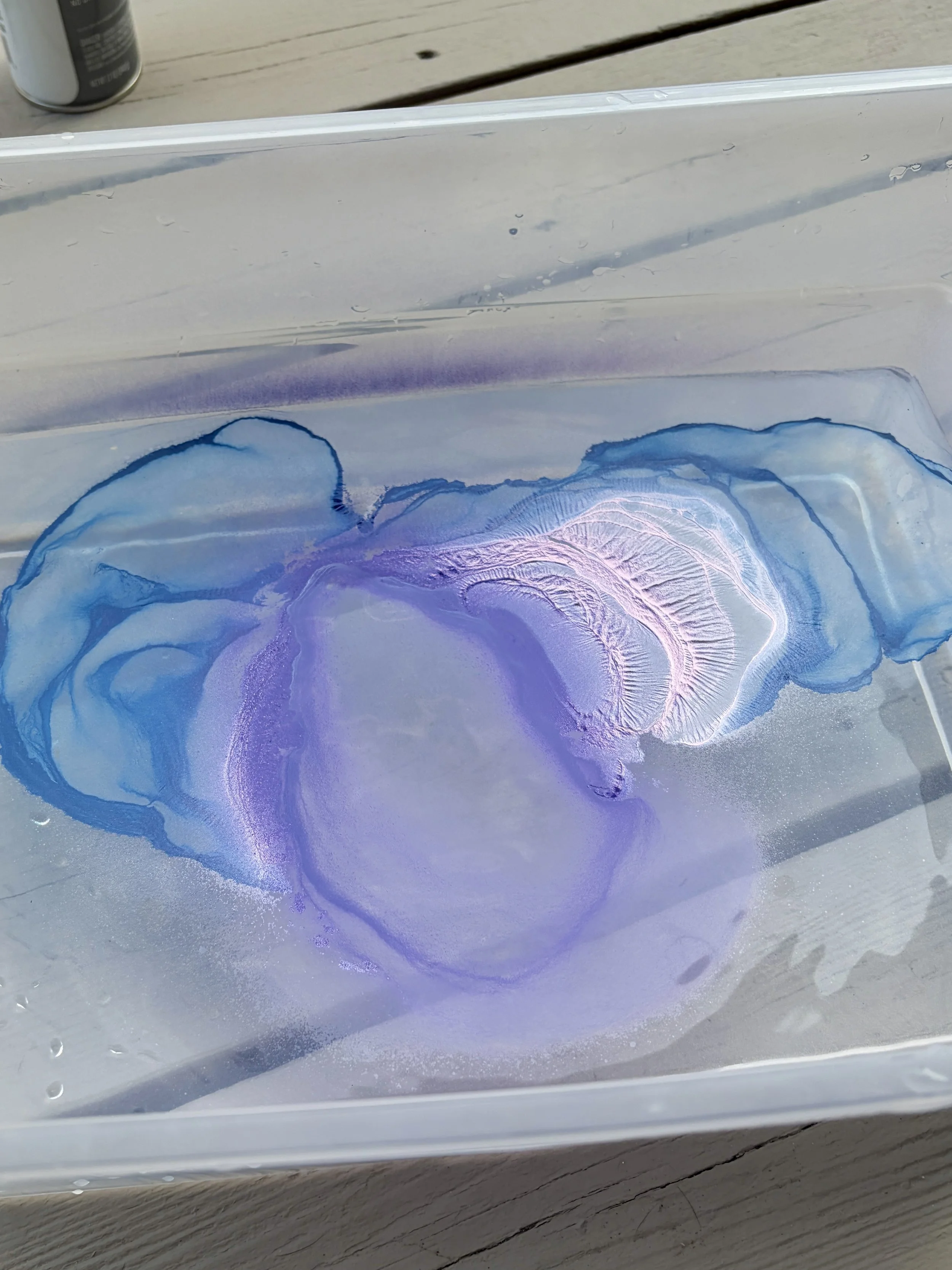 Blue and purple spray paint floating on water in a hydro dipping station before dipping a rock