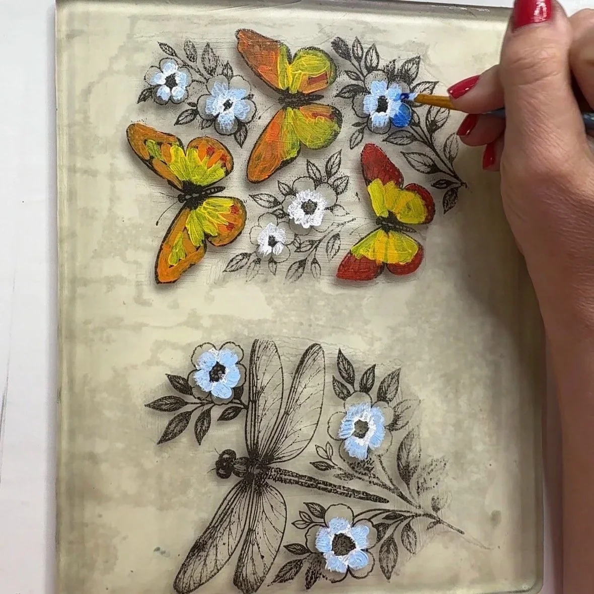 Hand painting orange and yellow acrylic paint onto a gelli plate transfer of butterflies and a dragonfly