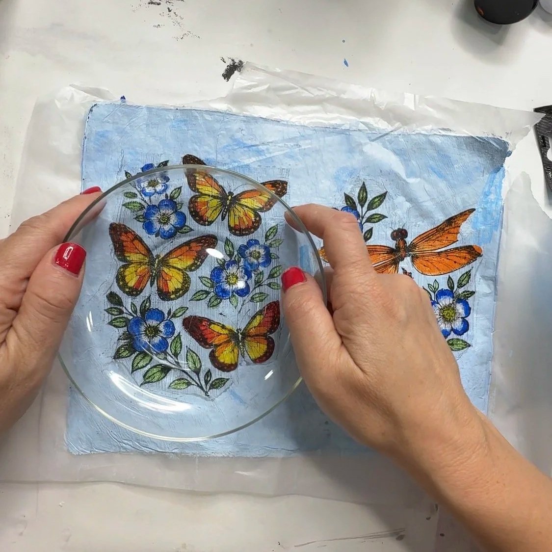 Positioning a glass bowl over arranged butterfly and floral tissue paper pieces to plan the layout