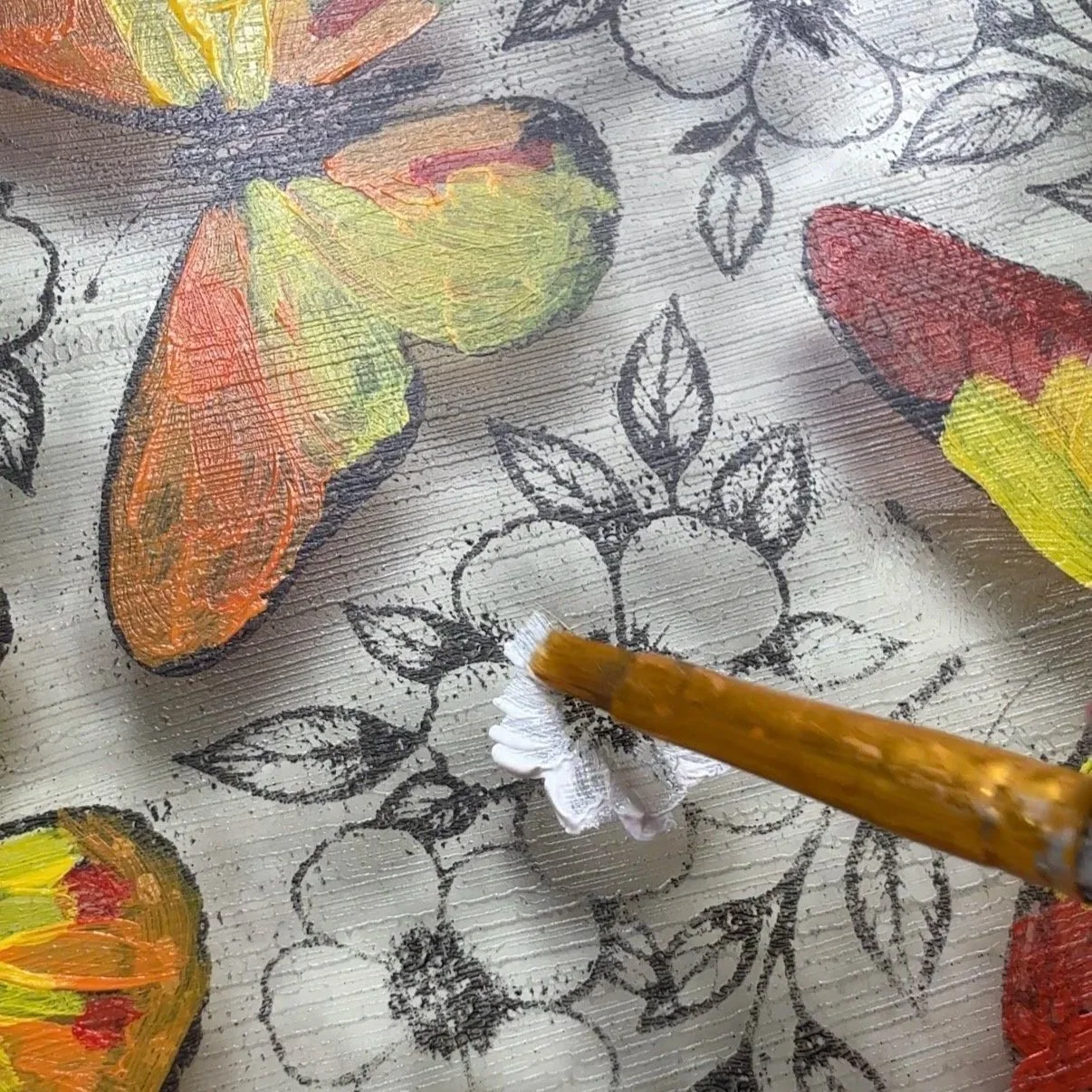 Close-up of a paintbrush adding white highlights to a blue flower on a gelli plate transfer