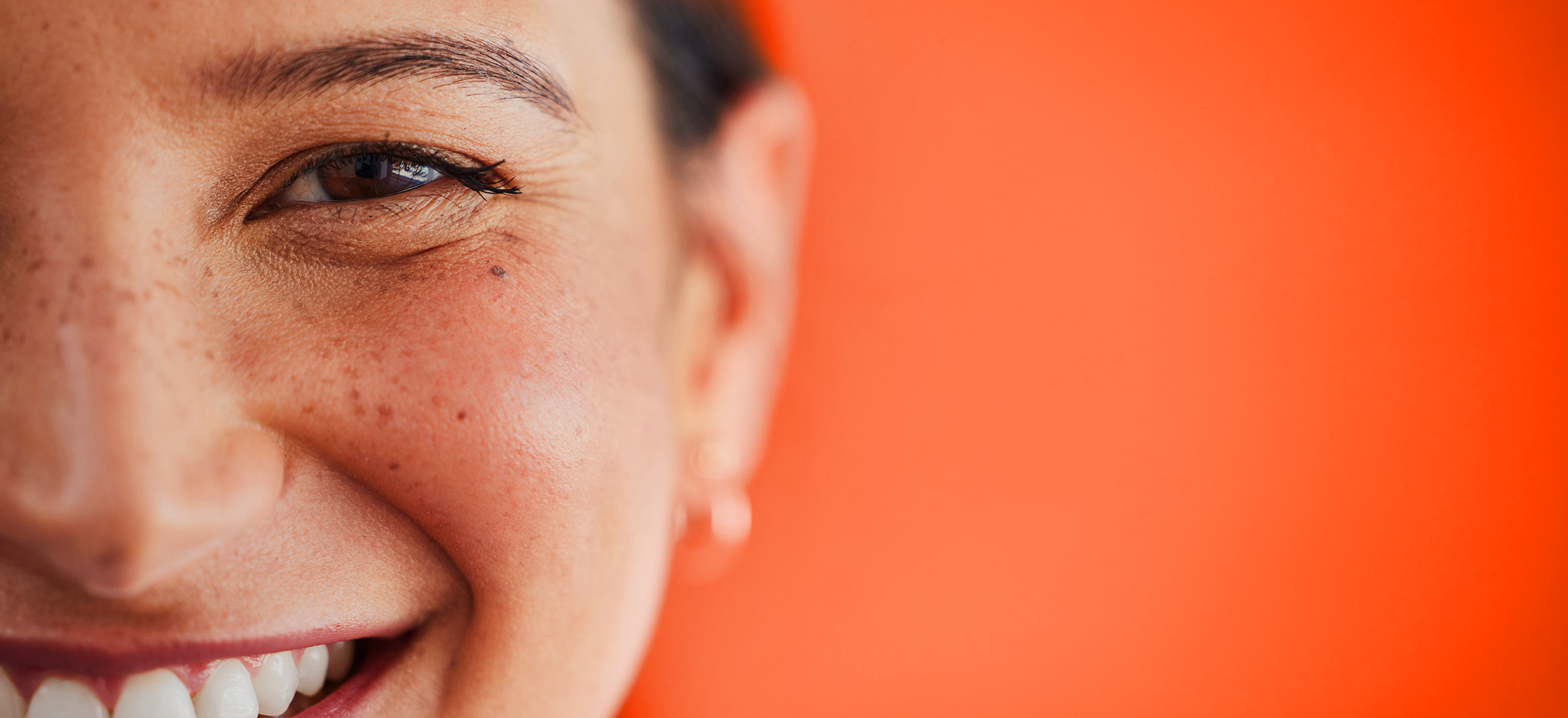 Close-up of a smiling person with freckles, orange background.
