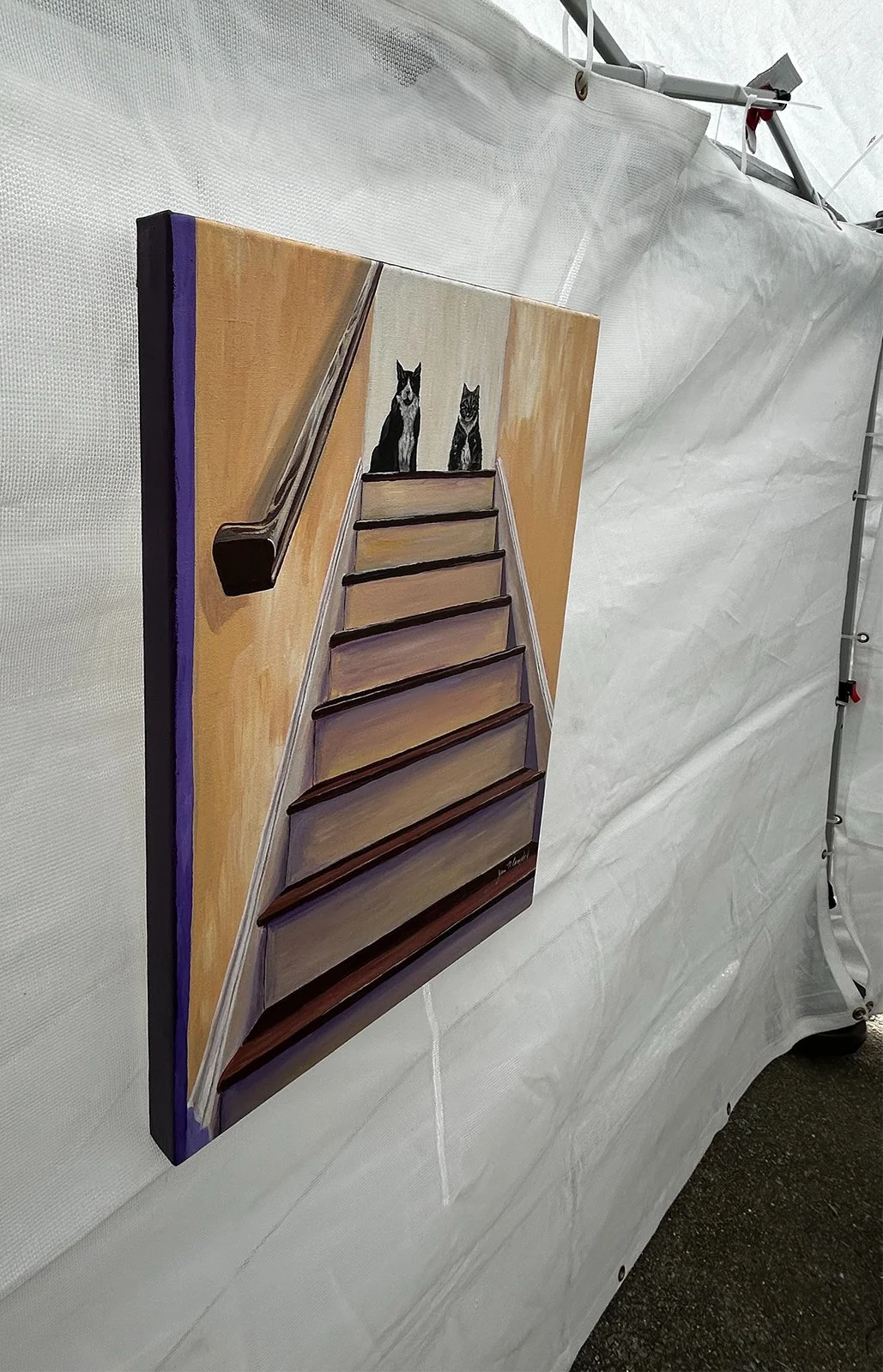Painting of two cats at the top of the stairs hanging inside a pop-up booth.