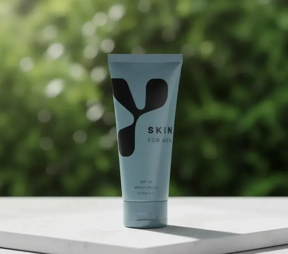 A tube of men's skincare product labeled 'Skin for Men' with SPF 40, moisturizer, and vitamin C, placed on a white surface outdoors with green leafy background.