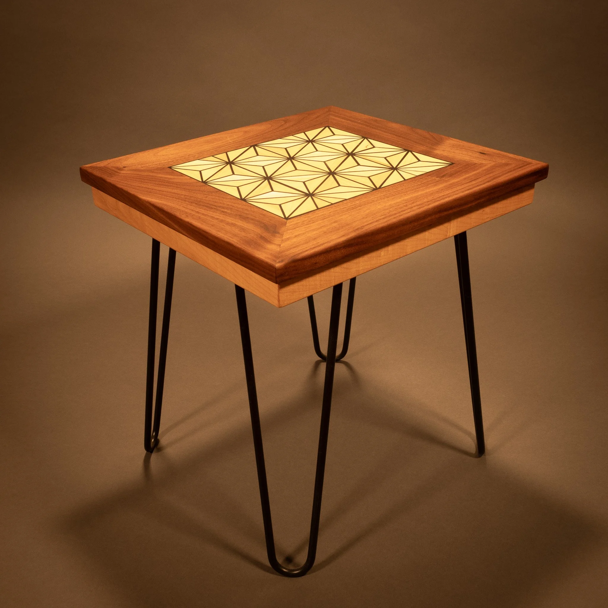 A modern wooden table with a geometric patterned light panel on top, supported by black metal legs, illuminated in a dark room.