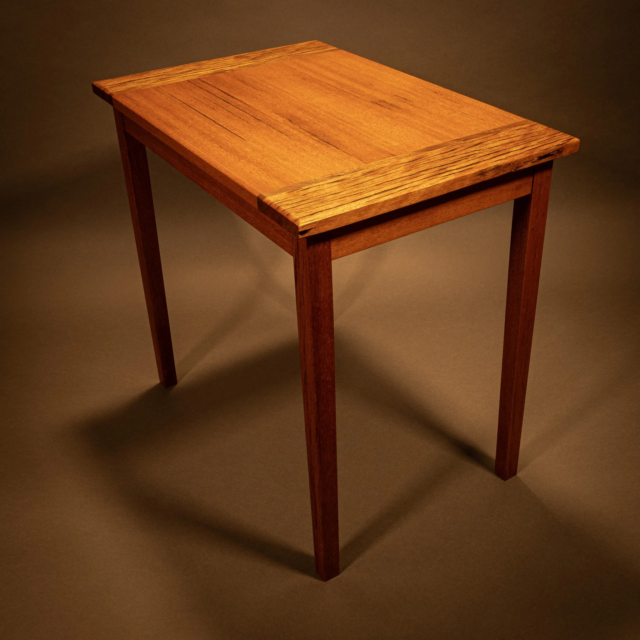 A wooden side table with a square top and four legs, set against a dark background.