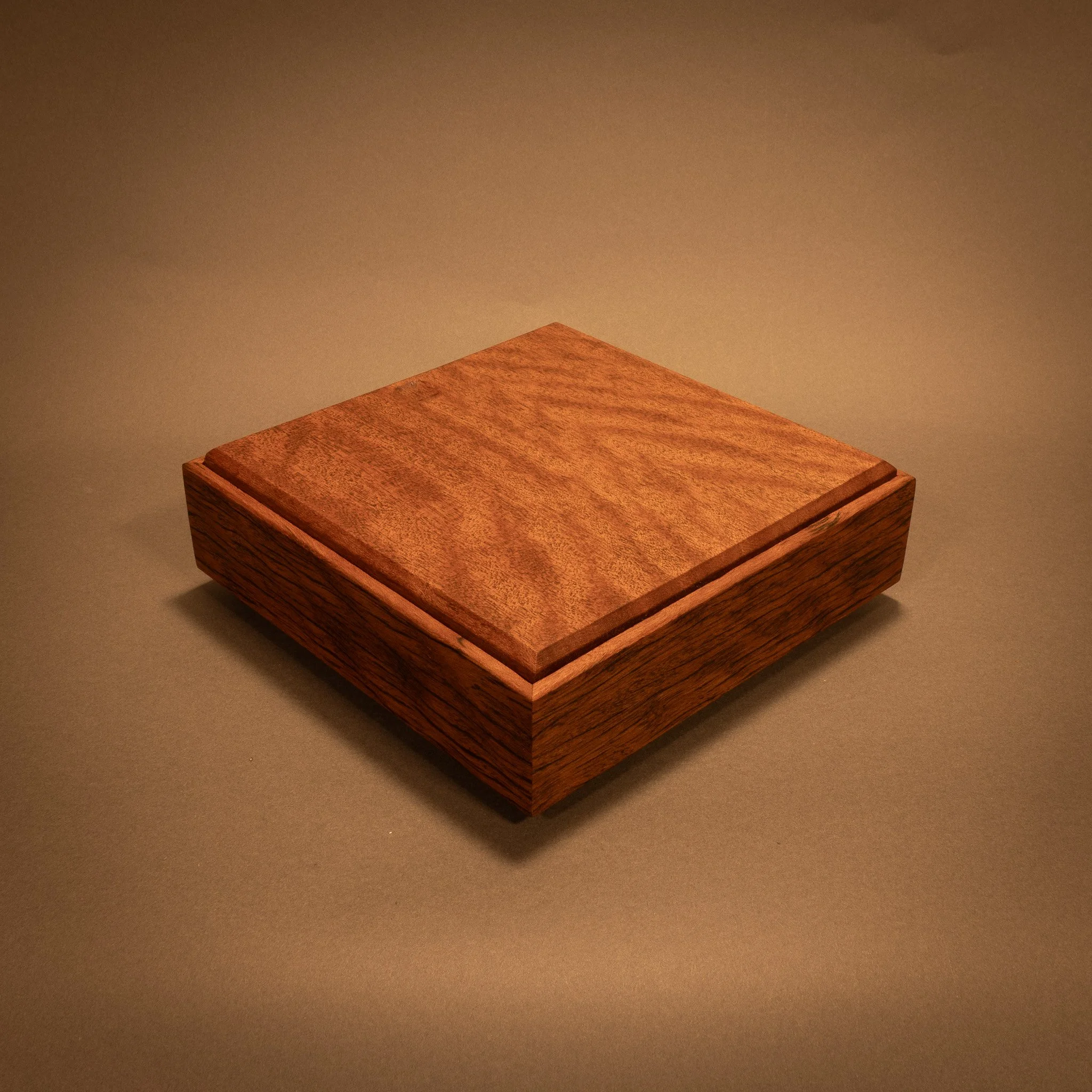 A wooden box with a natural finish placed on a plain, beige surface with a plain, beige background.