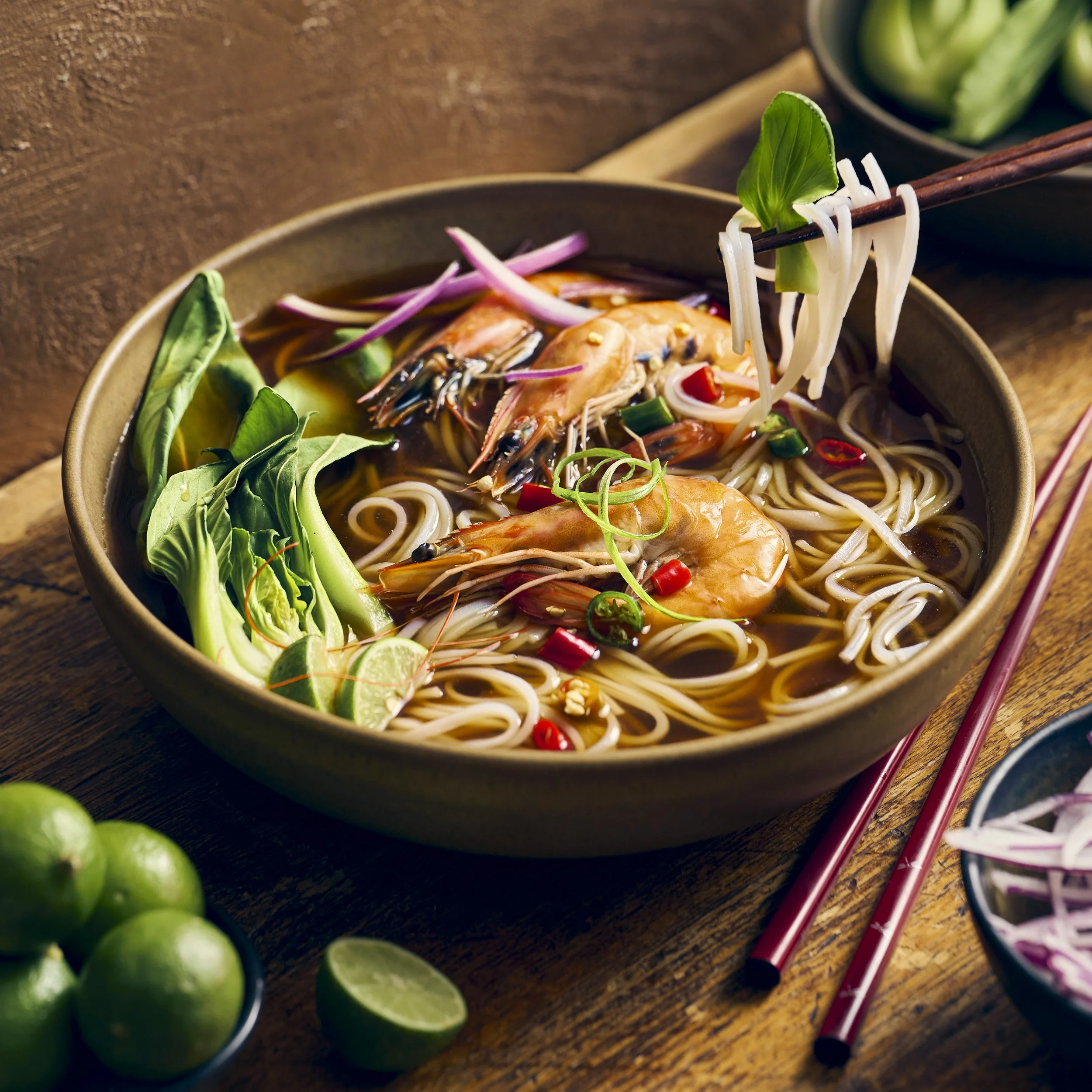 Pho shrimp noodle soup with bok choy, lime and chiles styled for commercial food photography.