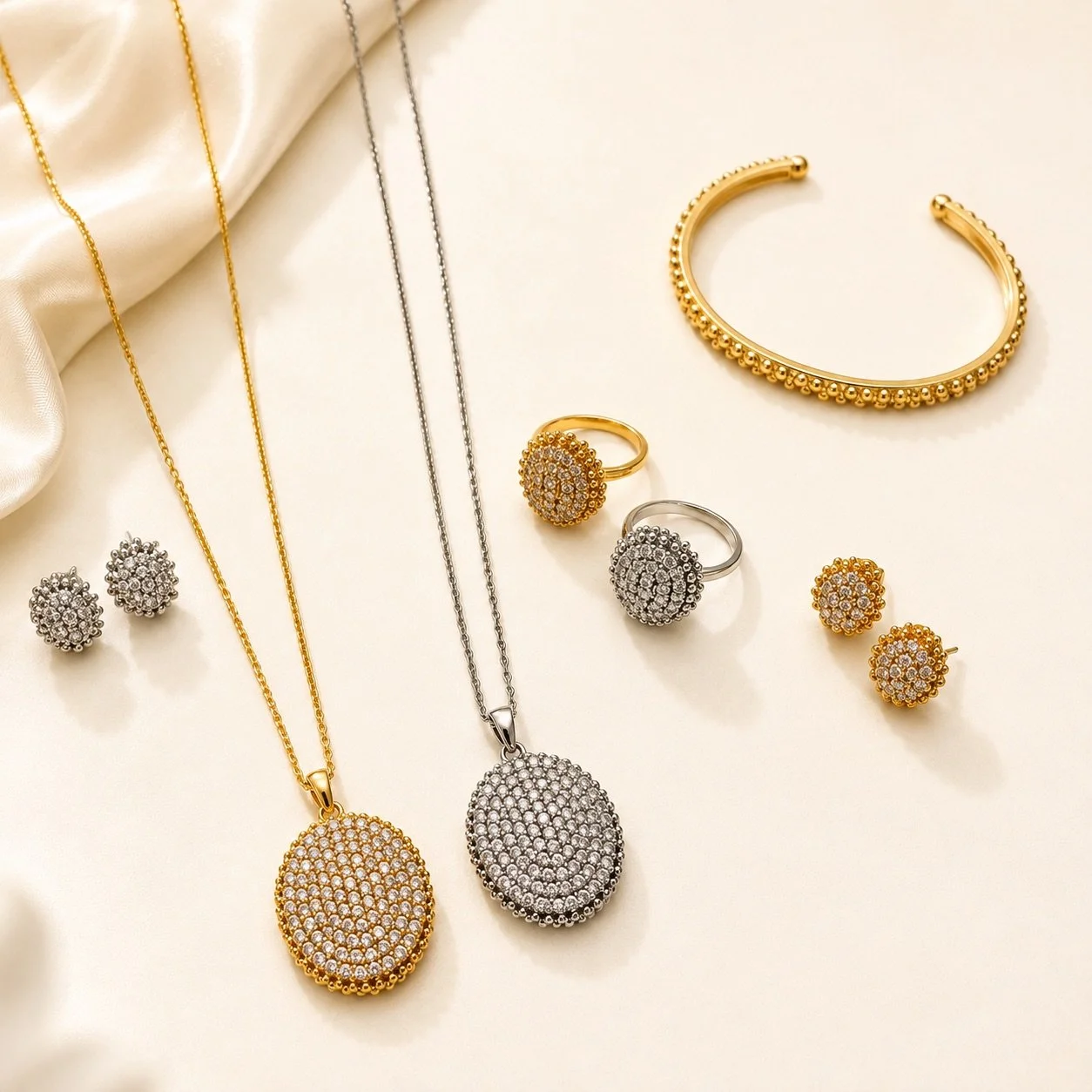 Gold and silver jewelry with diamond-like stones, including necklaces, earrings, rings, and a bracelet on a white surface with a satin cloth in the background.