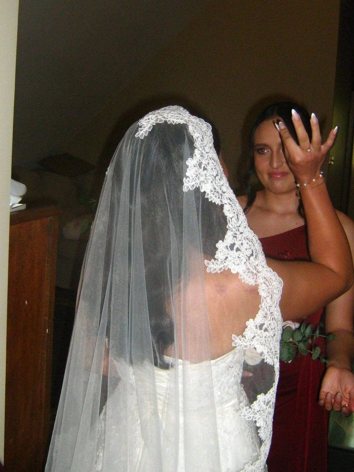 Woman applying makeup to bride with wedding veil and dress in indoor setting.