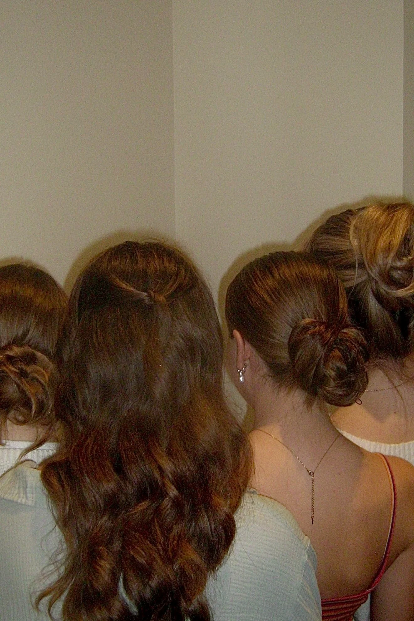 Group of women with styled hair gathered together, facing away from camera, in front of a plain wall.