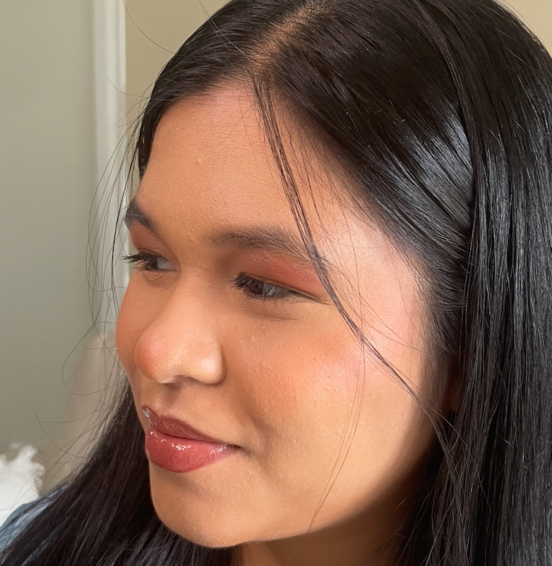 Close-up of a young woman with long black hair, wearing subtle makeup, looking down with a slight smile.