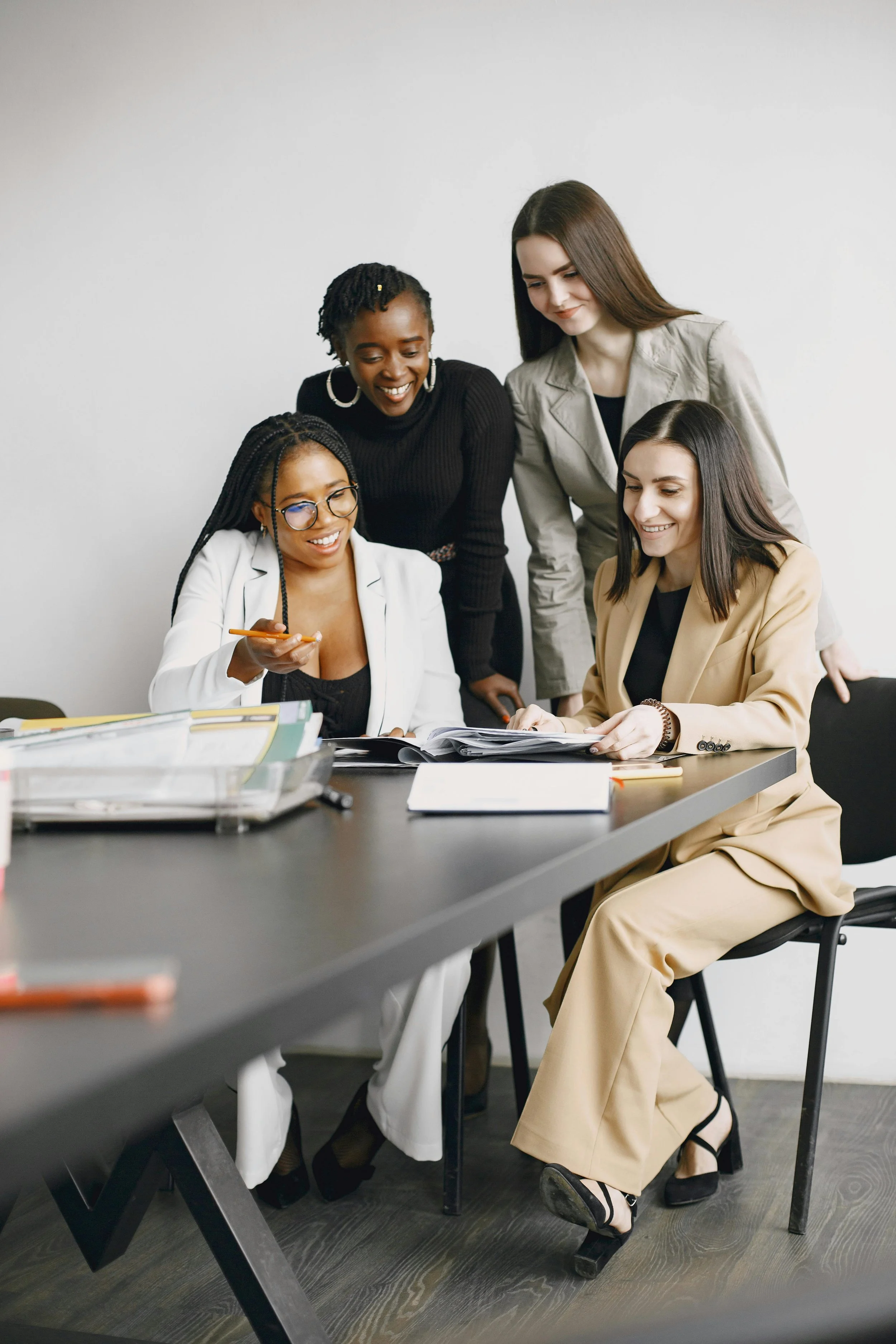 Four women of diverse backgrounds gathered around a table, looking at documents and smiling, in an office setting.