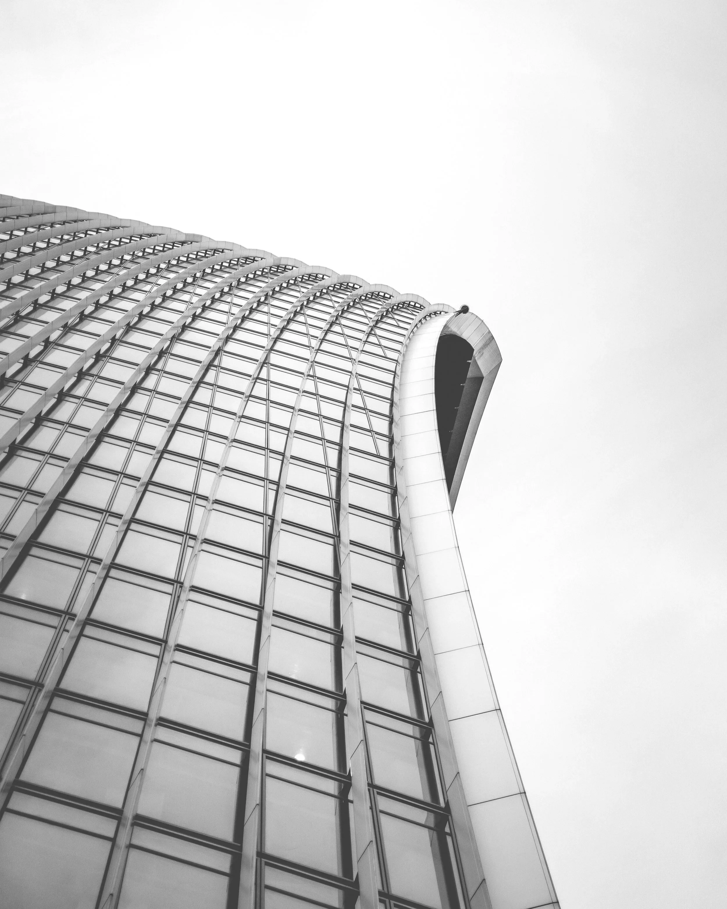 Low-angle view of a modern glass skyscraper with curved architectural design on overcast sky.