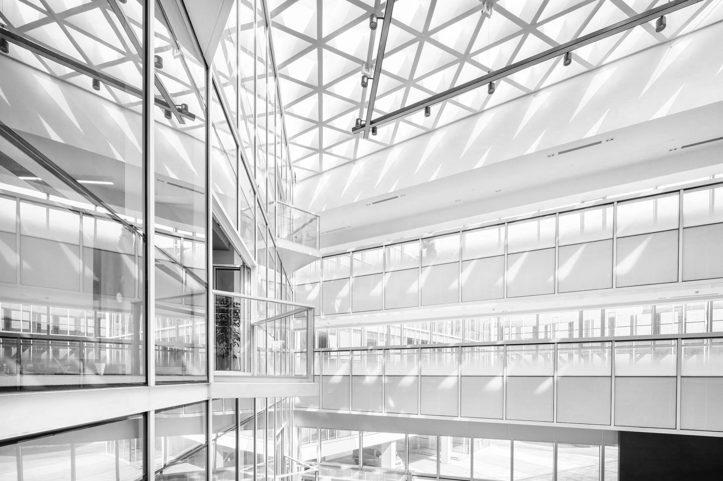 Modern multi-story building with glass walls, a glass ceiling with a geometric pattern, and shadows of the structure cast on the ceiling.