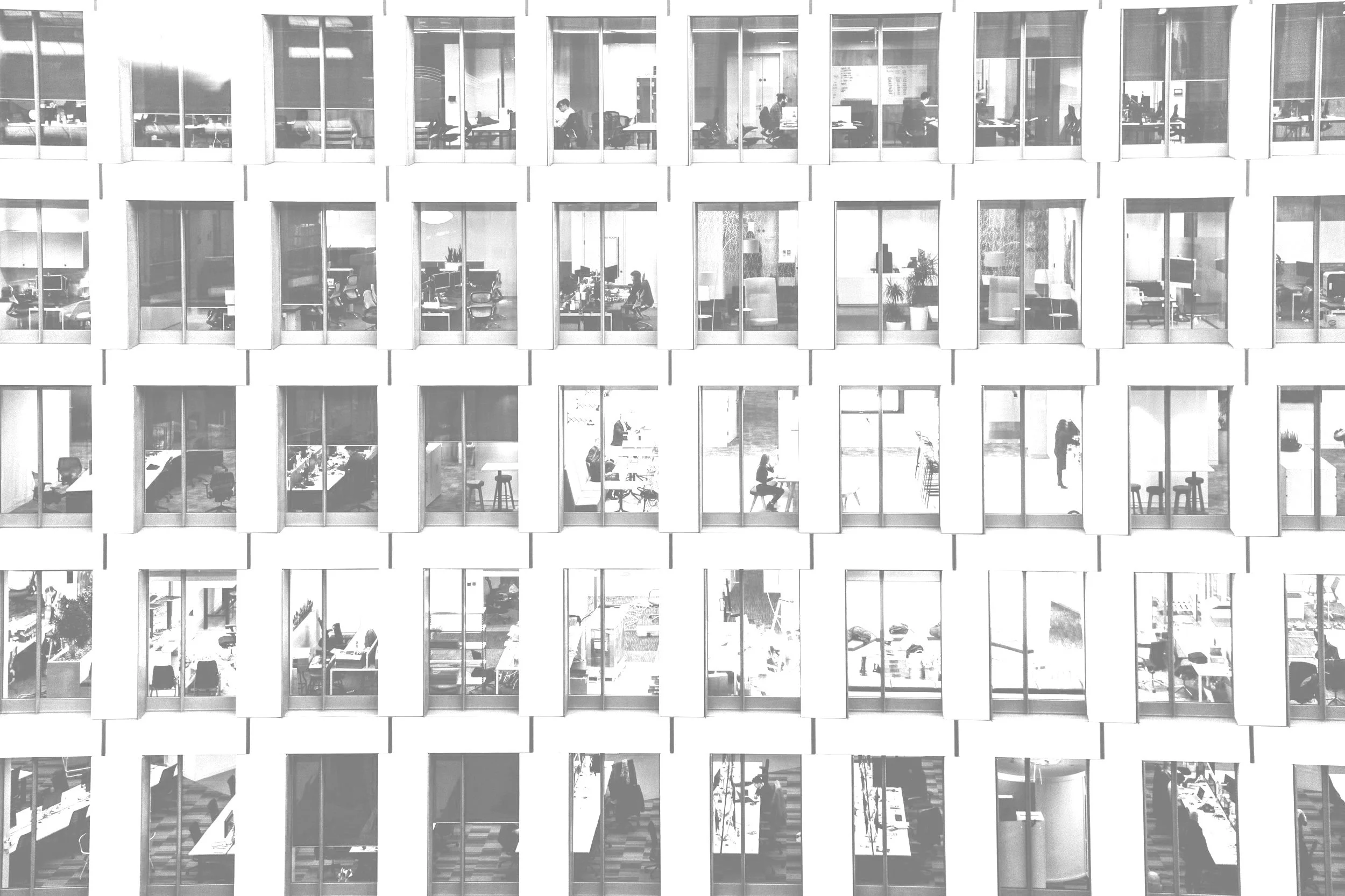 View of the exterior of a modern office building with multiple floors, each with large glass windows revealing office spaces and workers inside.