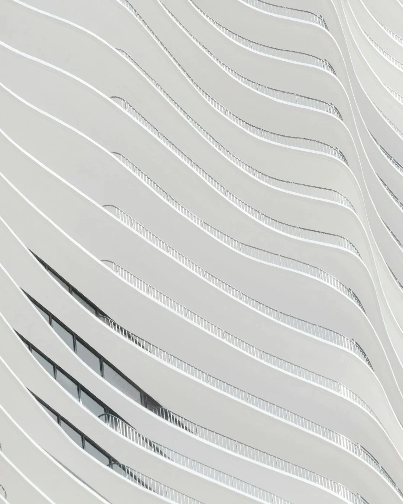 A modern high-rise building with a distinctive curved design and white exterior, featuring repeating balcony lines.