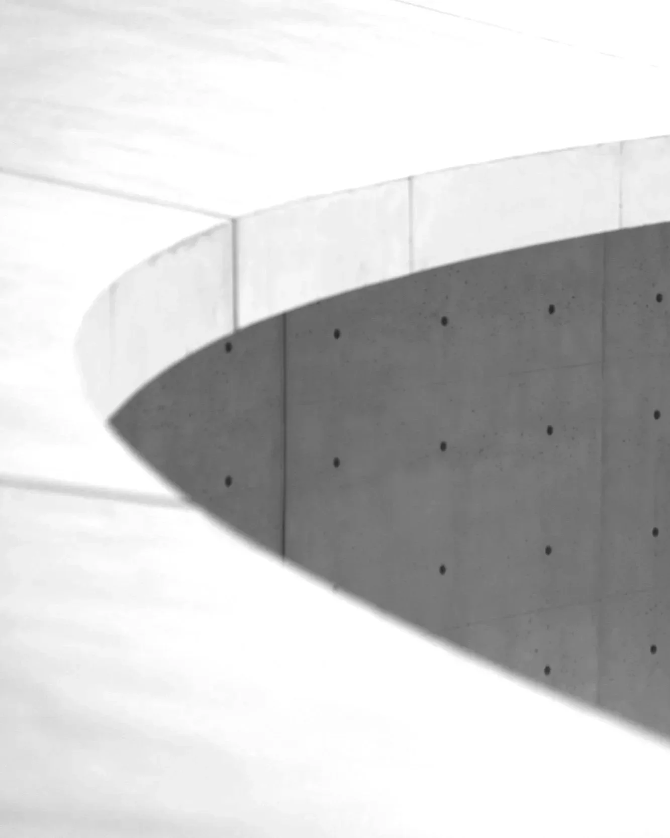 Close-up of a modern concrete building with a curved wall and small circular holes, in black and white.