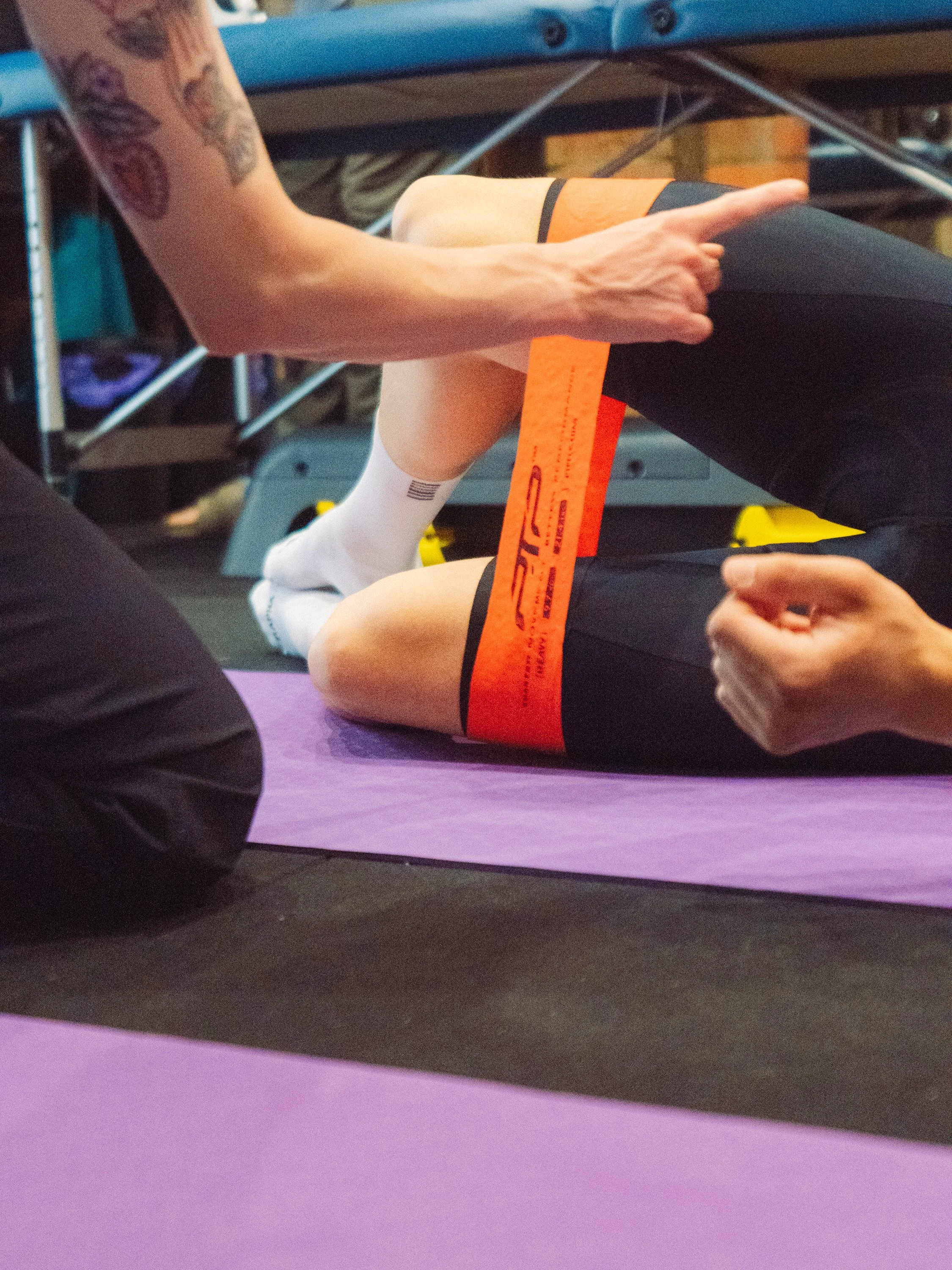 A person doing physical therapy exercises on a purple yoga mat, with a physical therapist assisting, wearing black shorts and white socks.
