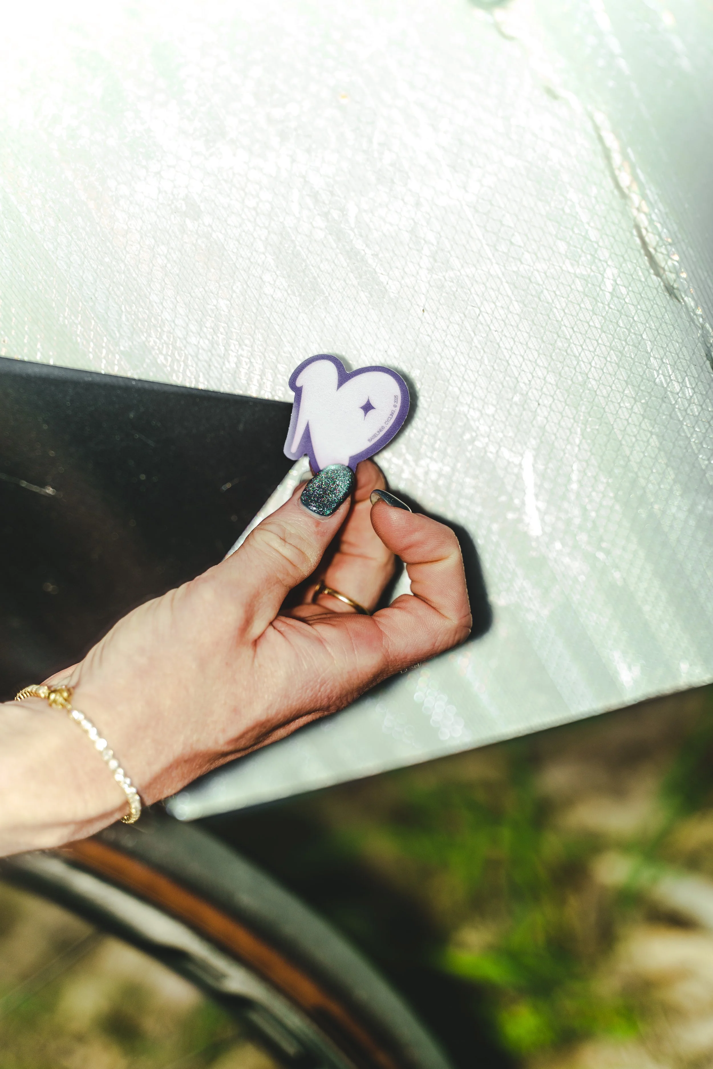 Person holding a sticker with a silhouette of a dog and a star, wearing a glittery nail polish, with a glittery background.