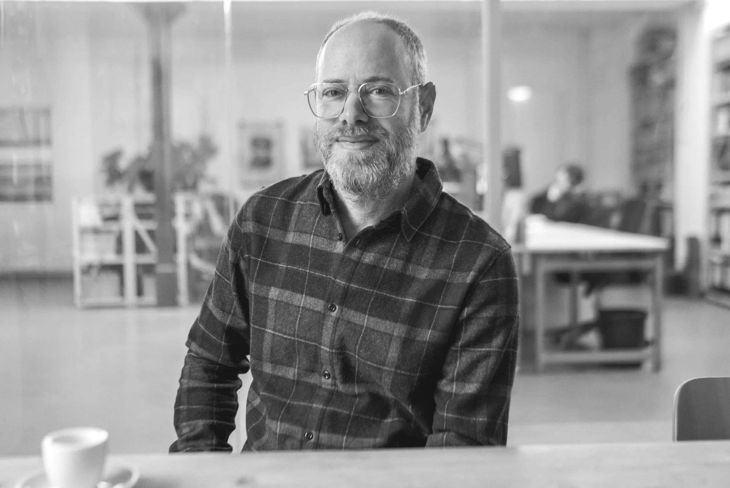 A middle-aged man with glasses, a beard, and a checked shirt sitting at a table in a library.