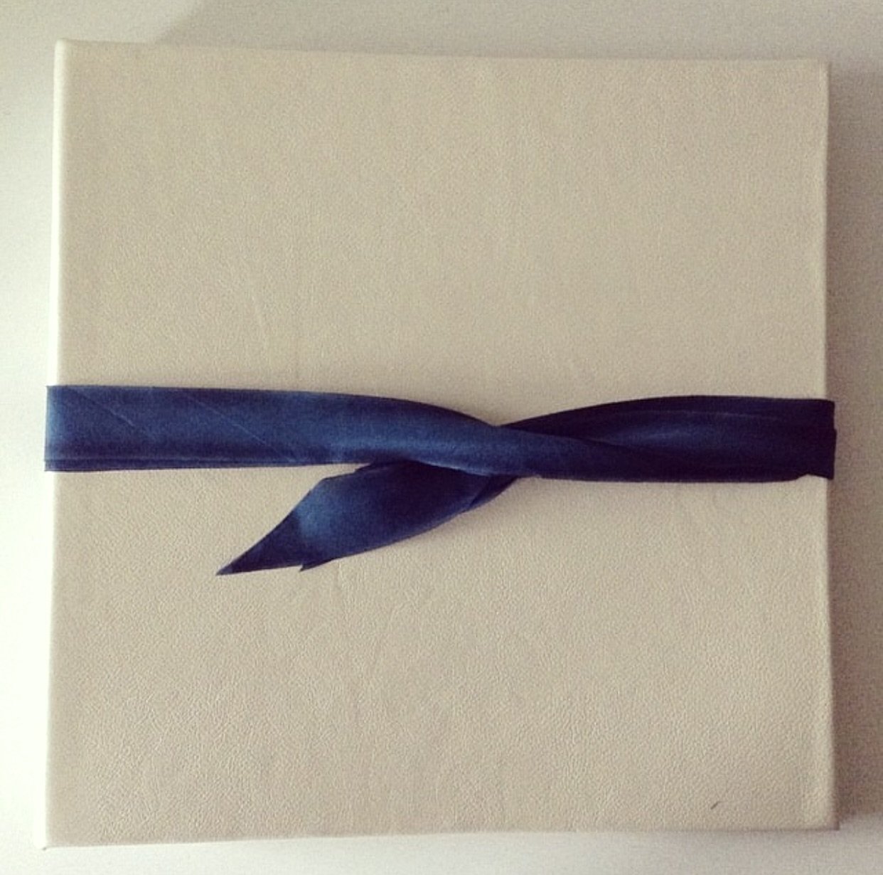 Wedding album covered in cream leather and wrapped with a silk ribbon. 14" square.