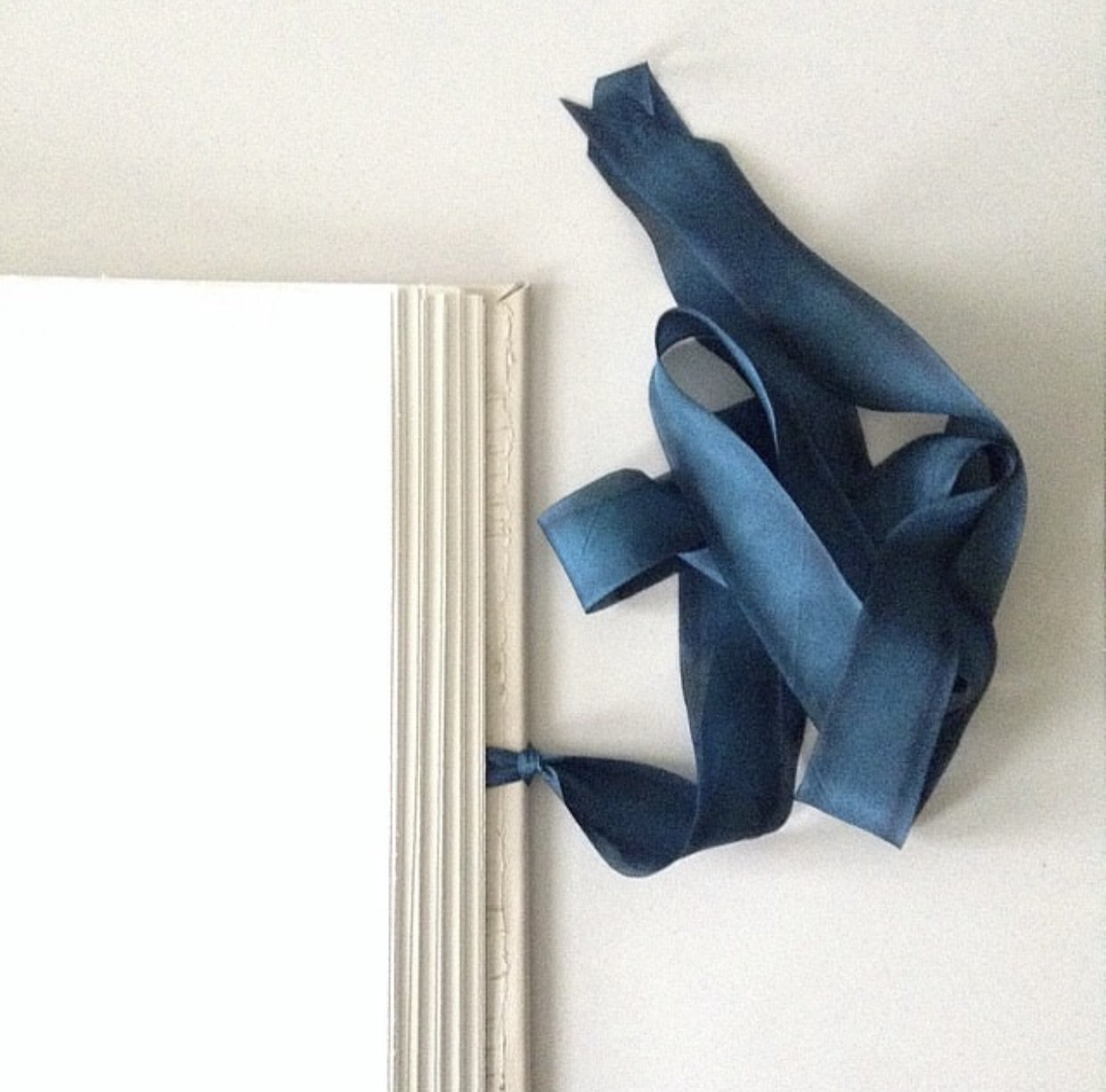 Wedding album covered in cream leather and wrapped with a silk ribbon. 14" square.