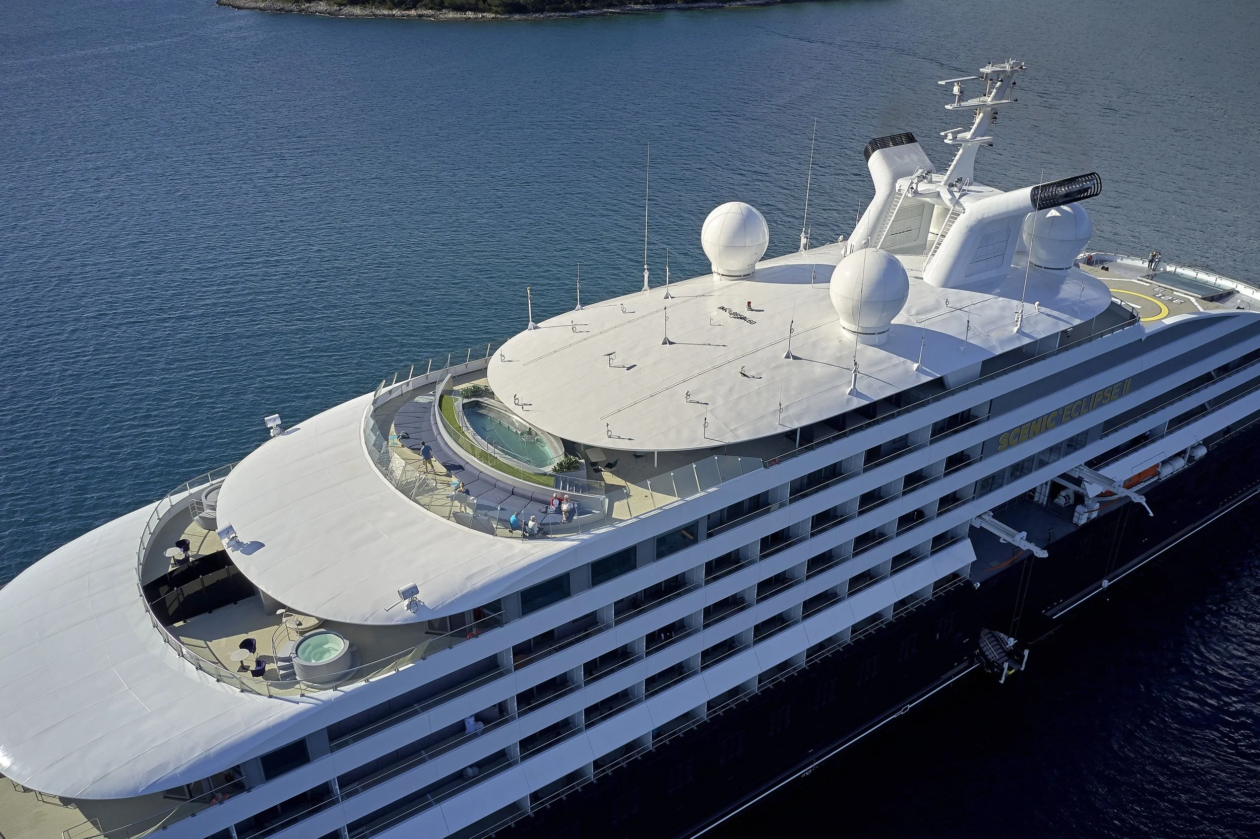 Ein Kreuzfahrtschiff mit einem weißen, modernen Oberdeck, das ein kleiner Pool, Sonnenliegen, Sonnen Schirme und Besucher bietet, befindet sich auf dem Meer