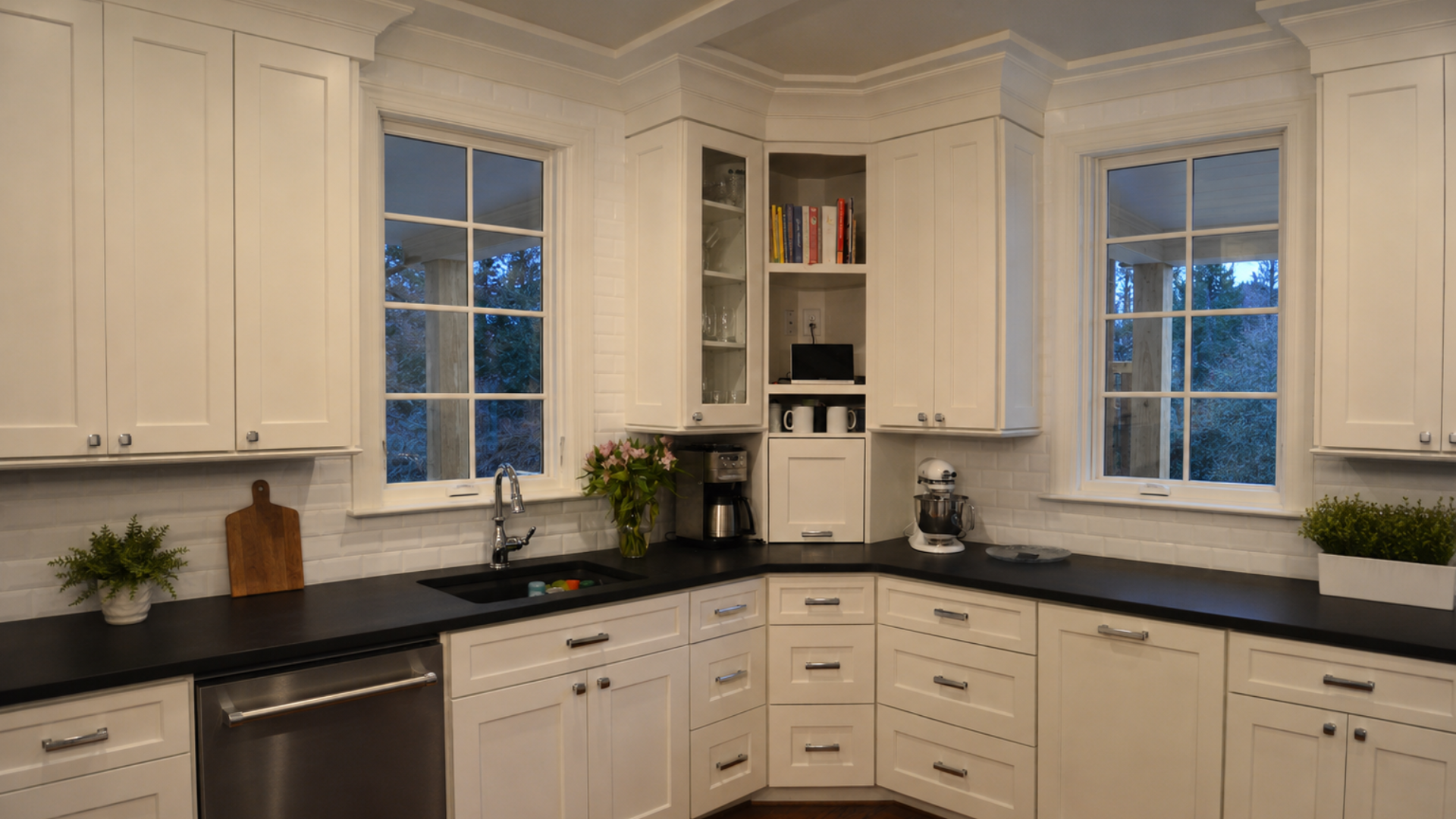 Deep blue-green kitchen cabinetry with a diagonal glass-front corner cabinet, brass hardware, and farmhouse sink.